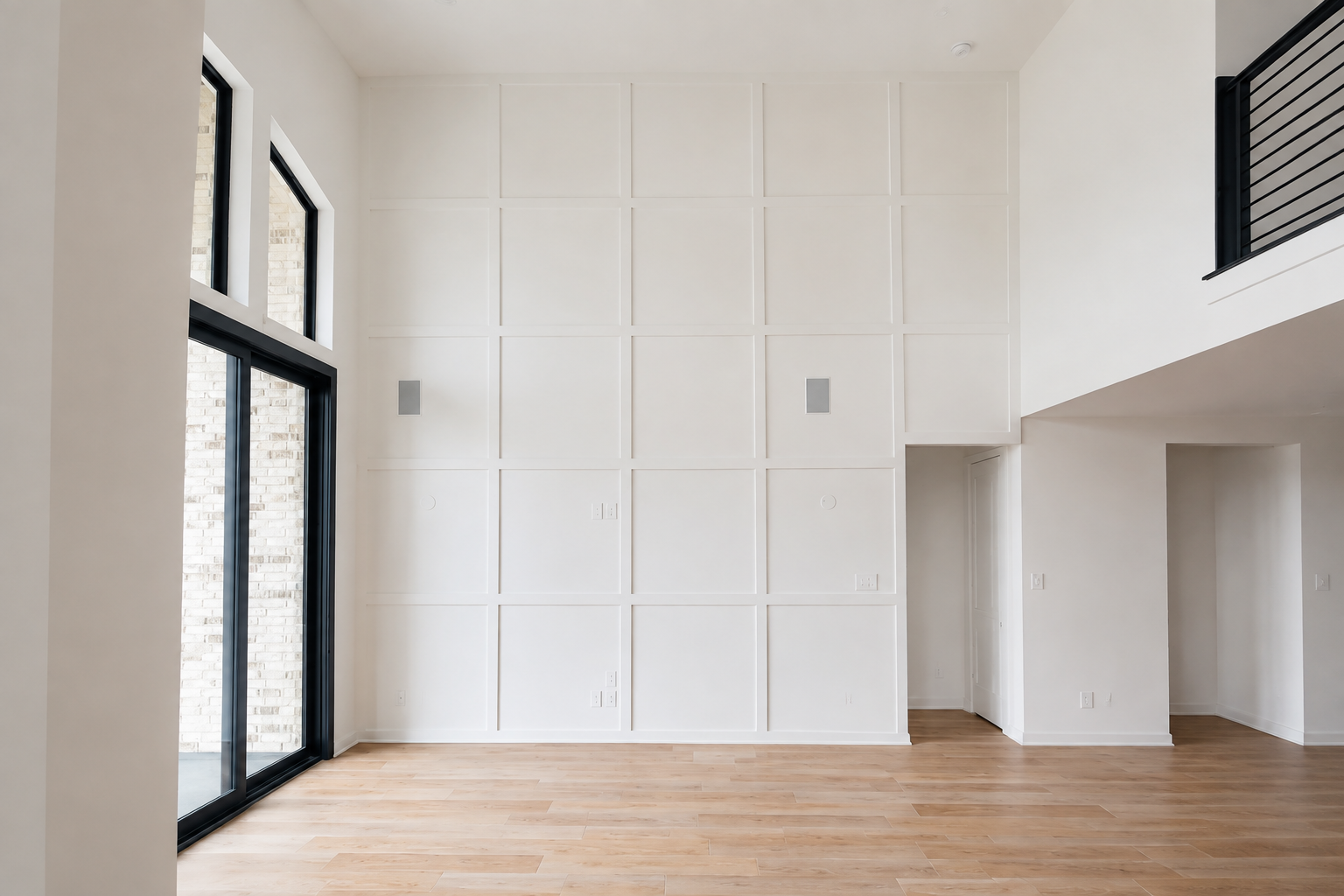 Empty modern room with wood floor, tall tan paneled wall, and large windows.