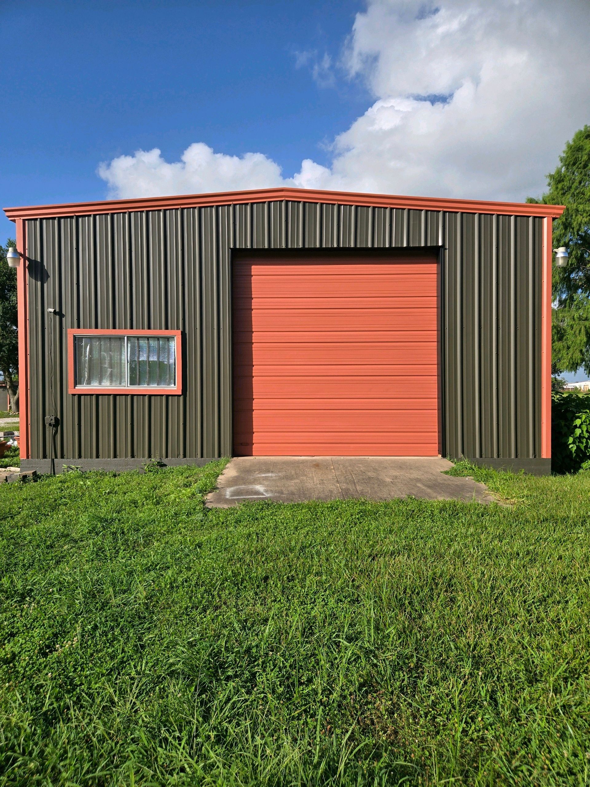 Small metal shed with red door and window, fronted by grass under a blue sky.