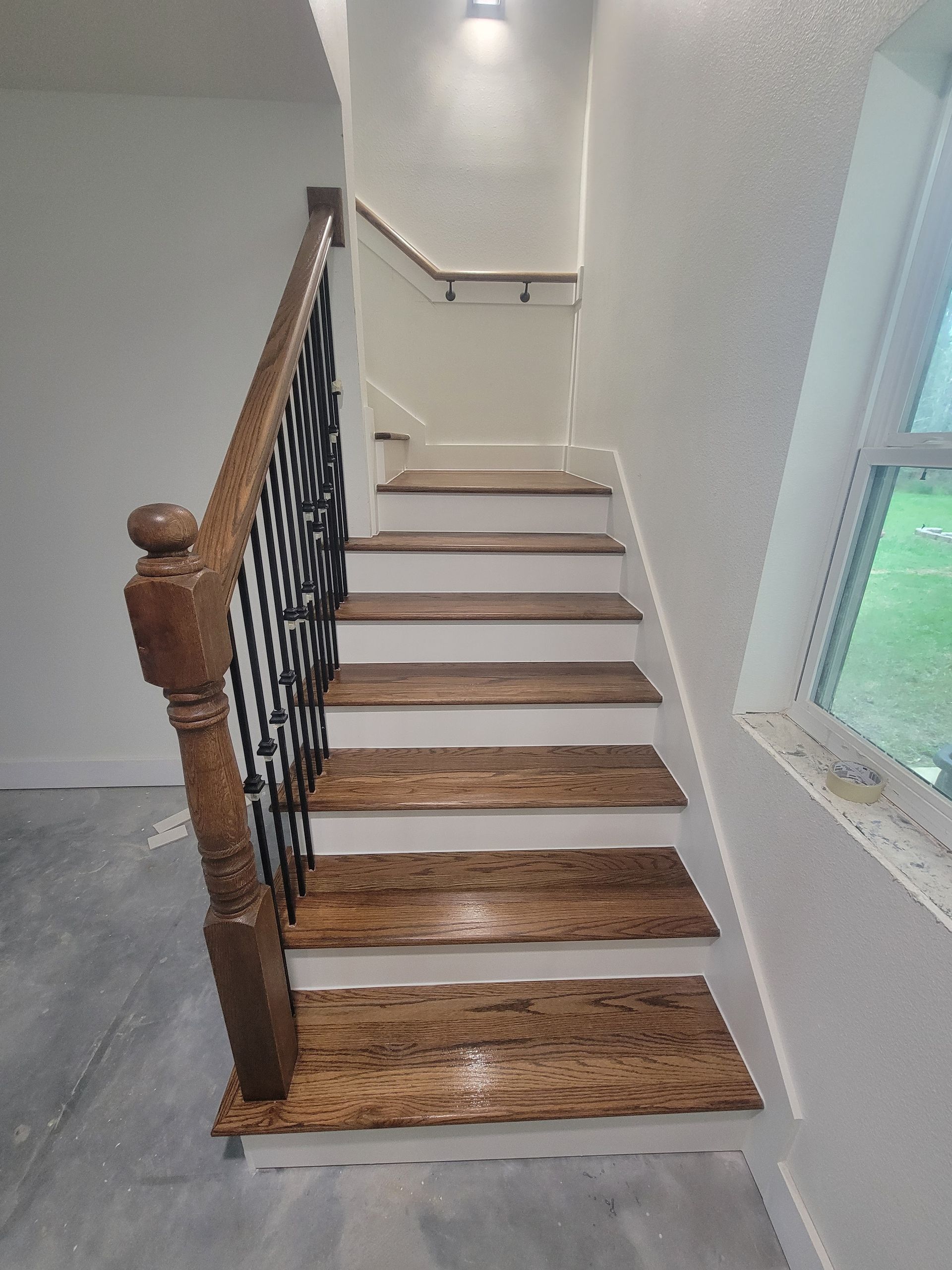 Indoor staircase with wooden steps, black iron railing, and white walls by a window