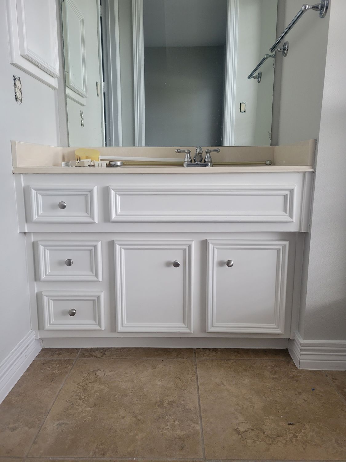 White bathroom vanity with sink and mirror, beige tiled floor, and a chrome towel bar on the right.