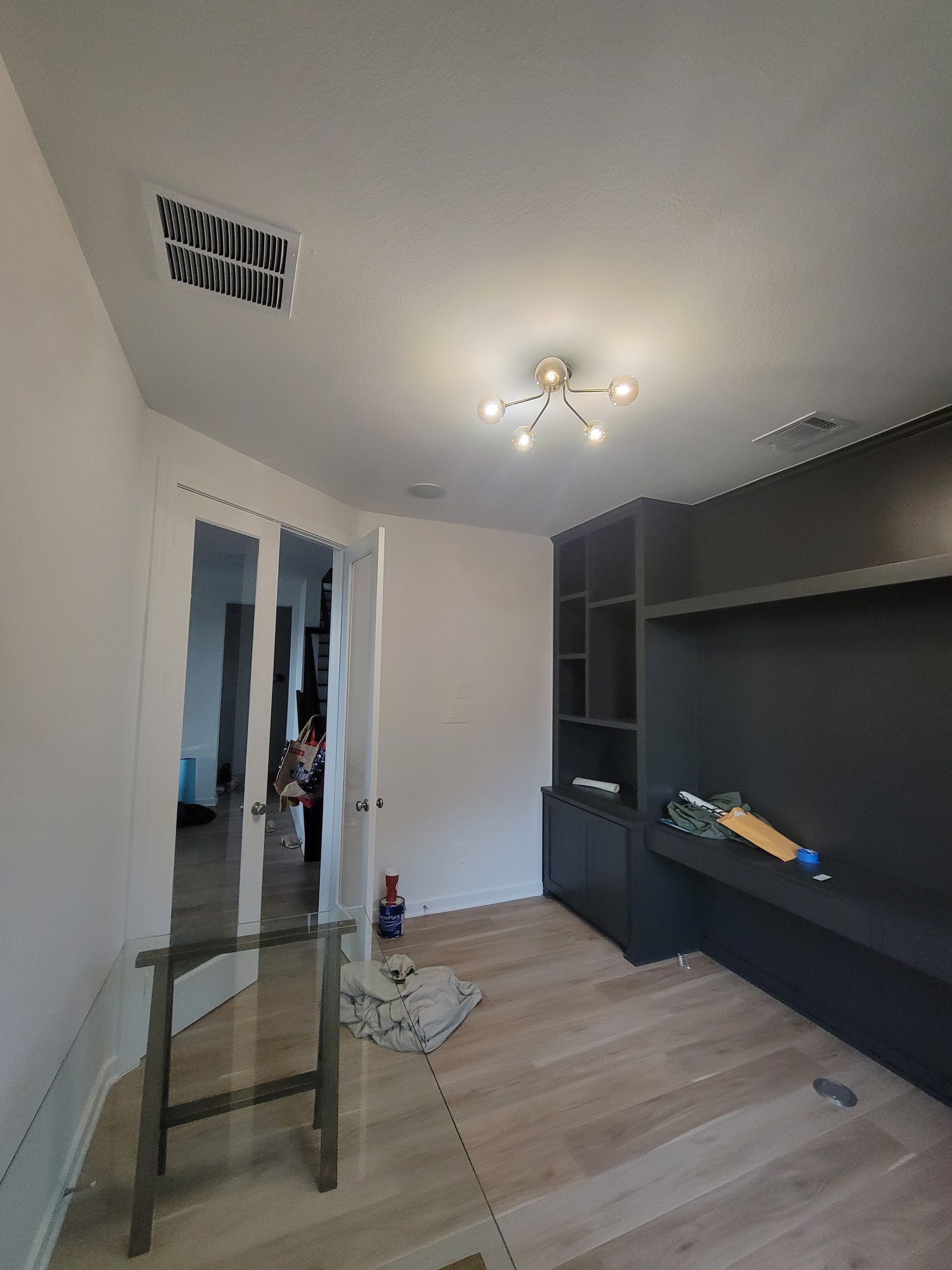 Empty room with light wood floor, white walls, ceiling light, and dark built-in shelving.