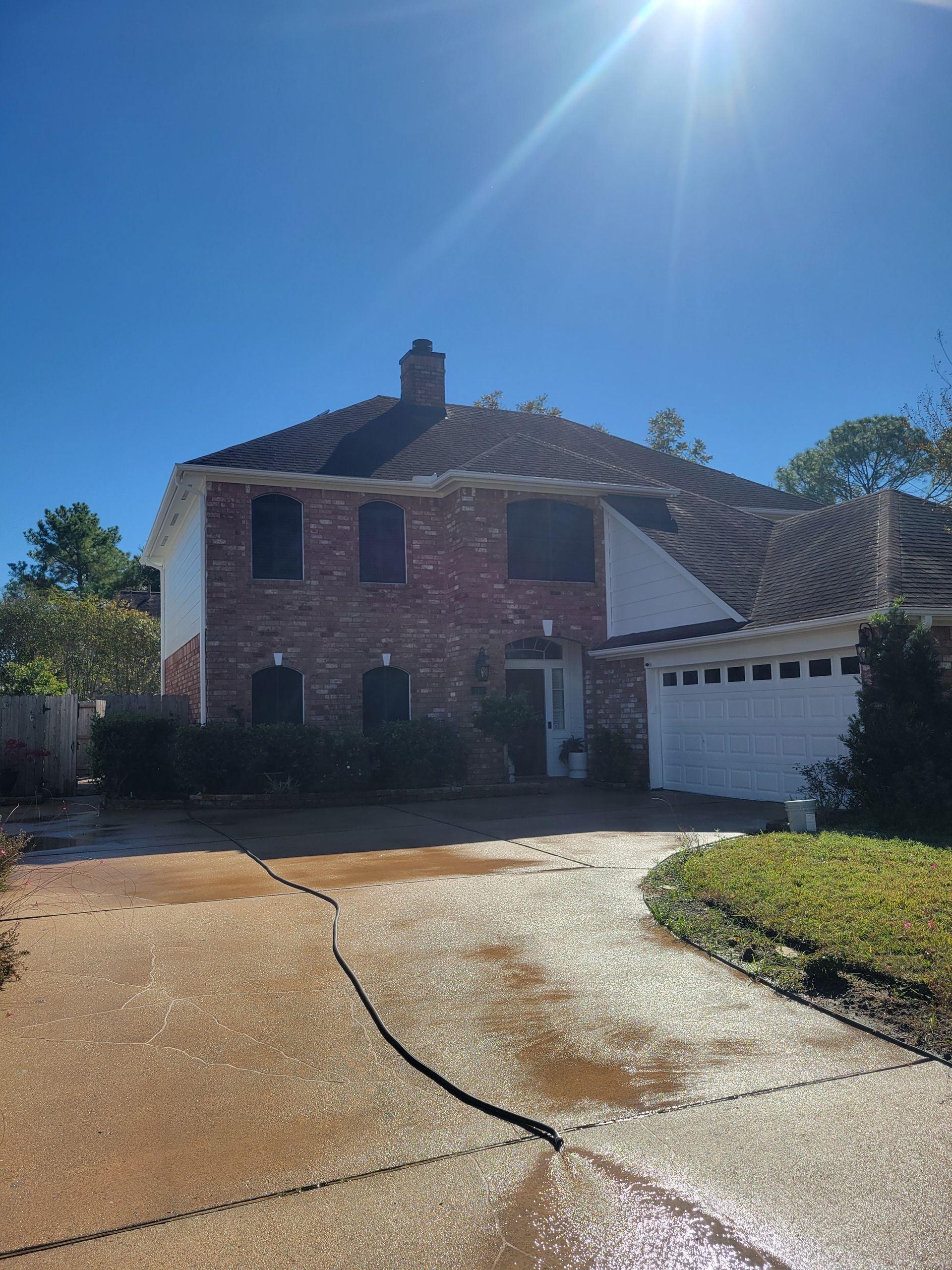 Two-story brick house with a white garage, sunlit driveway, and blue sky overhead