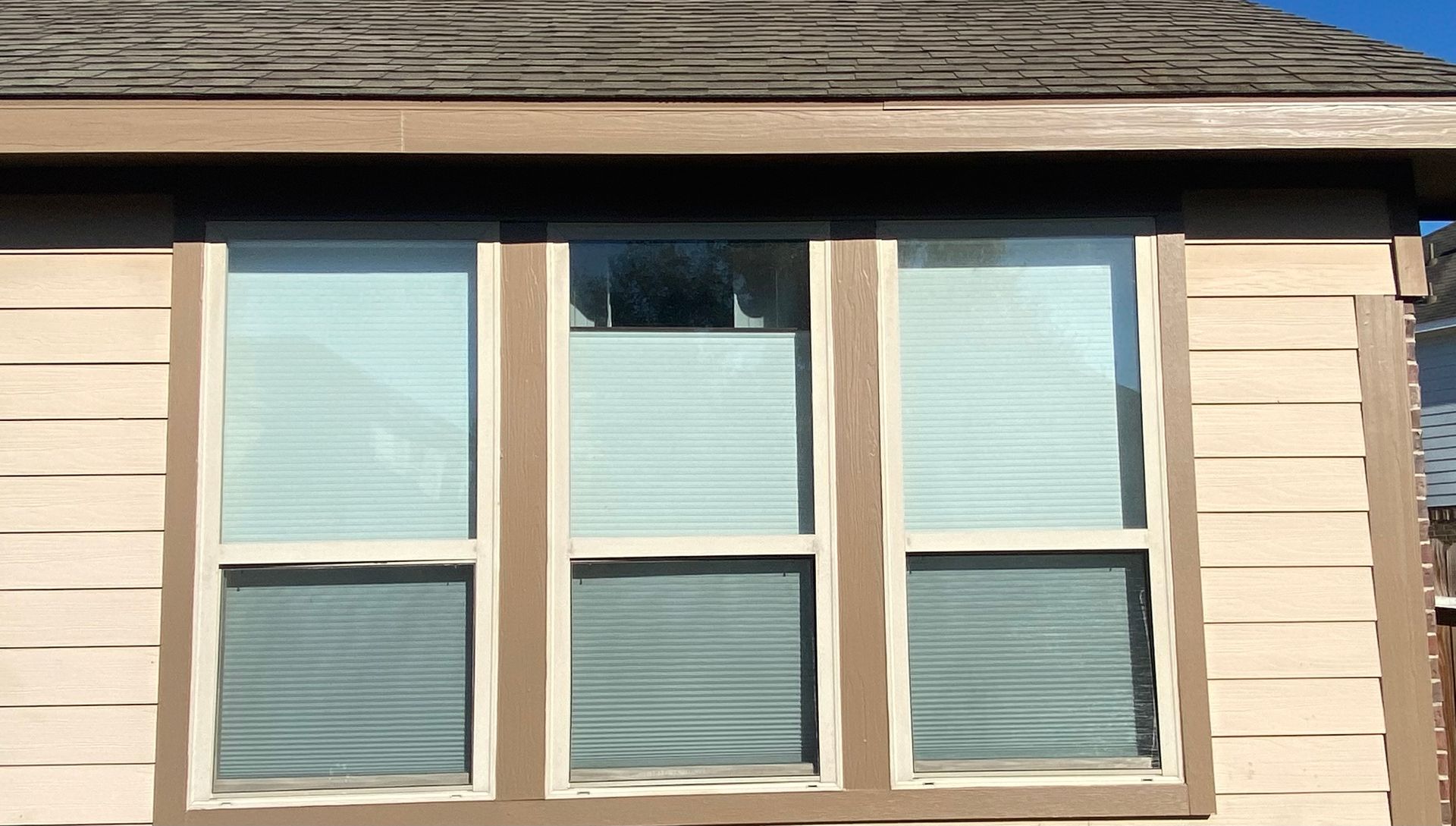 Three beige-trimmed windows on a beige house exterior under a shingled roofline