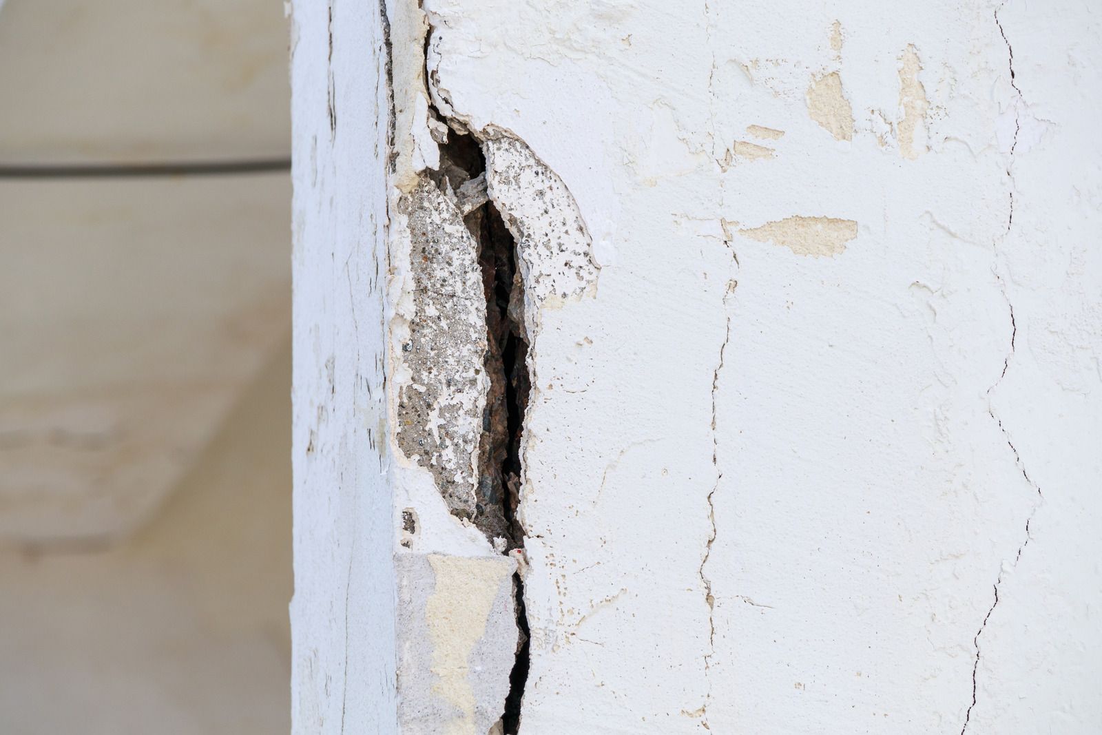 Close-up of a cracked white wall with a large chipped, peeling section exposing dark damage underneath
