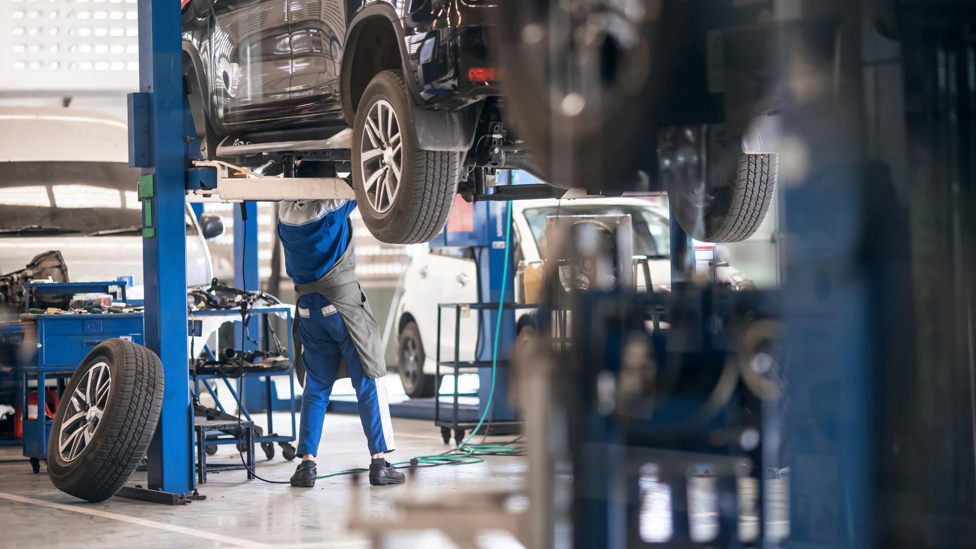 A man is working on a car on a lift in a garage.