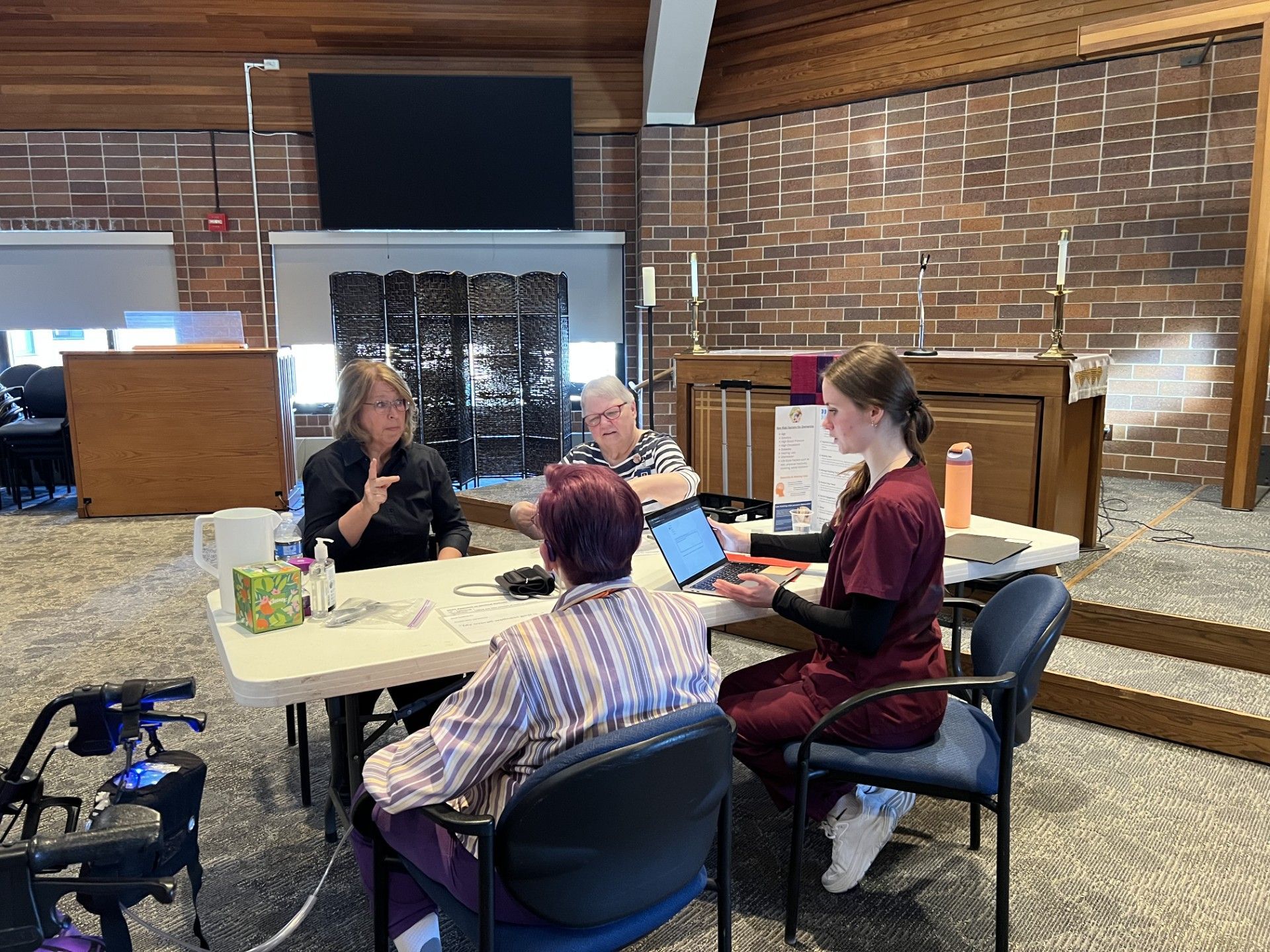 4 people sitting at table. Nurse and nursing student discussing wellness with deaf older adult, ASL interpreter present.