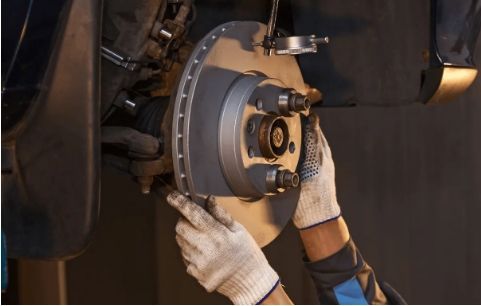Mechanic working on a car brake rotor with gloved hands in a garage