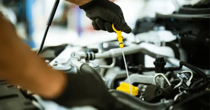 Mechanic using a yellow dipstick to inspect a car engine in a garage