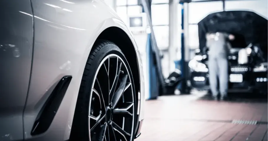White car wheel in a garage, with a second vehicle blurred in the background.