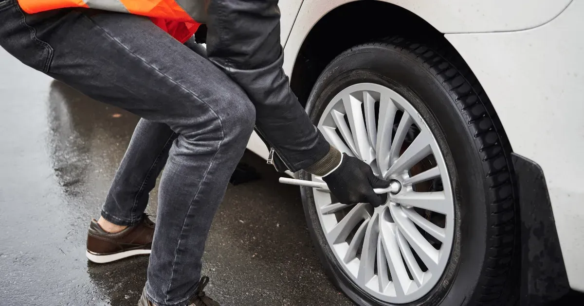 Person using a wheel wrench to change a car tire in the rain