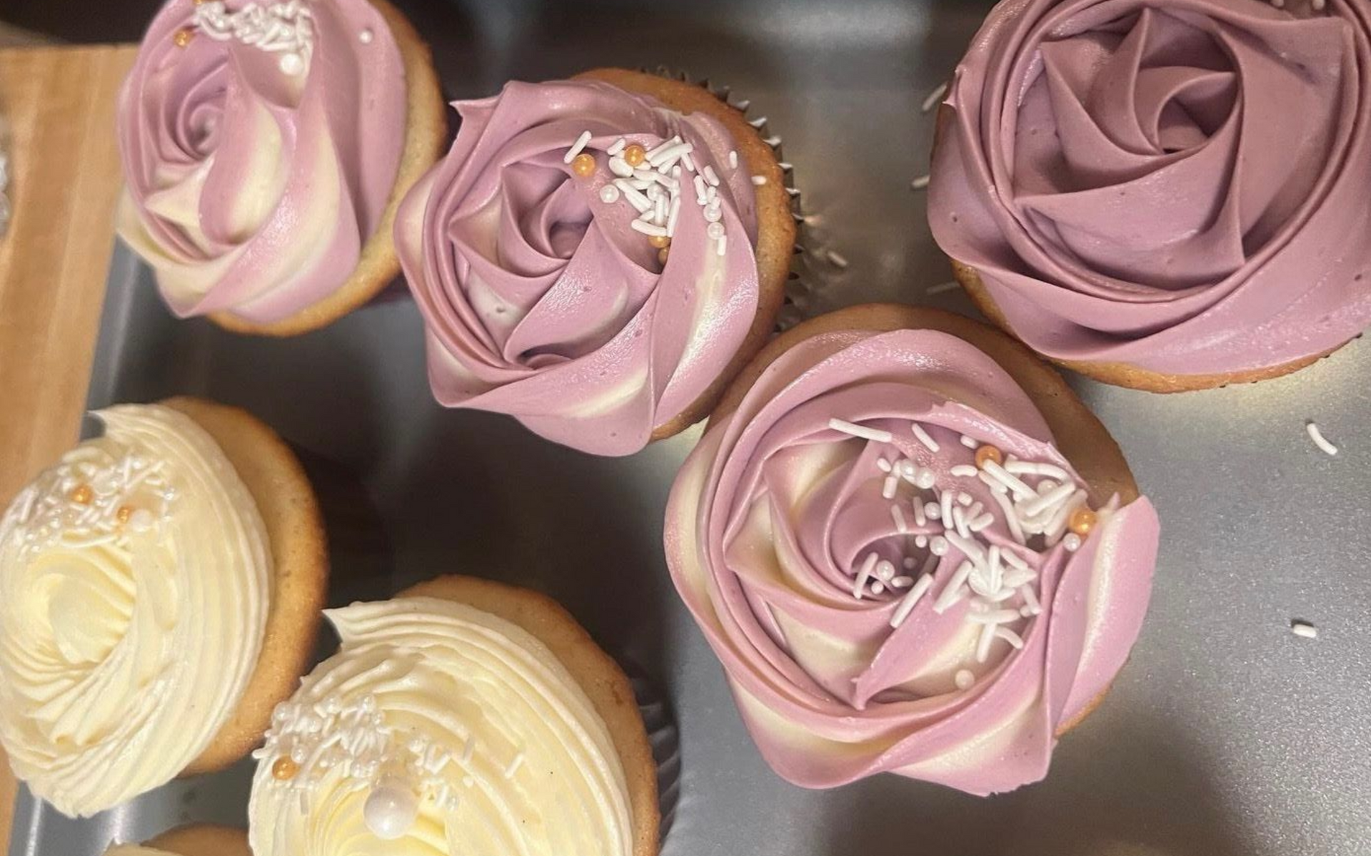 Assorted frosted cupcakes with pink and cream swirls on a tray, topped with sprinkles