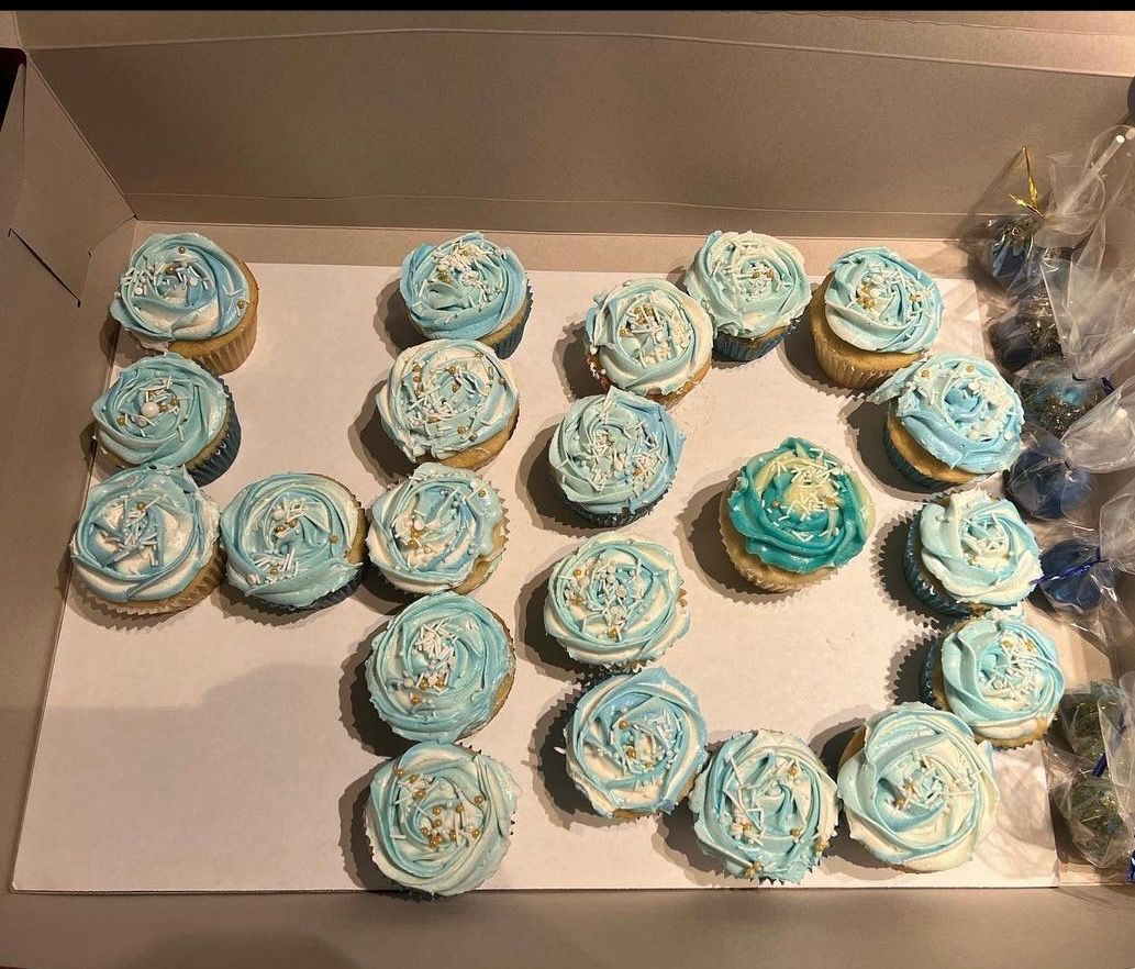 Box of blue-frosted cupcakes arranged in rows, with one teal cupcake near the center-right.