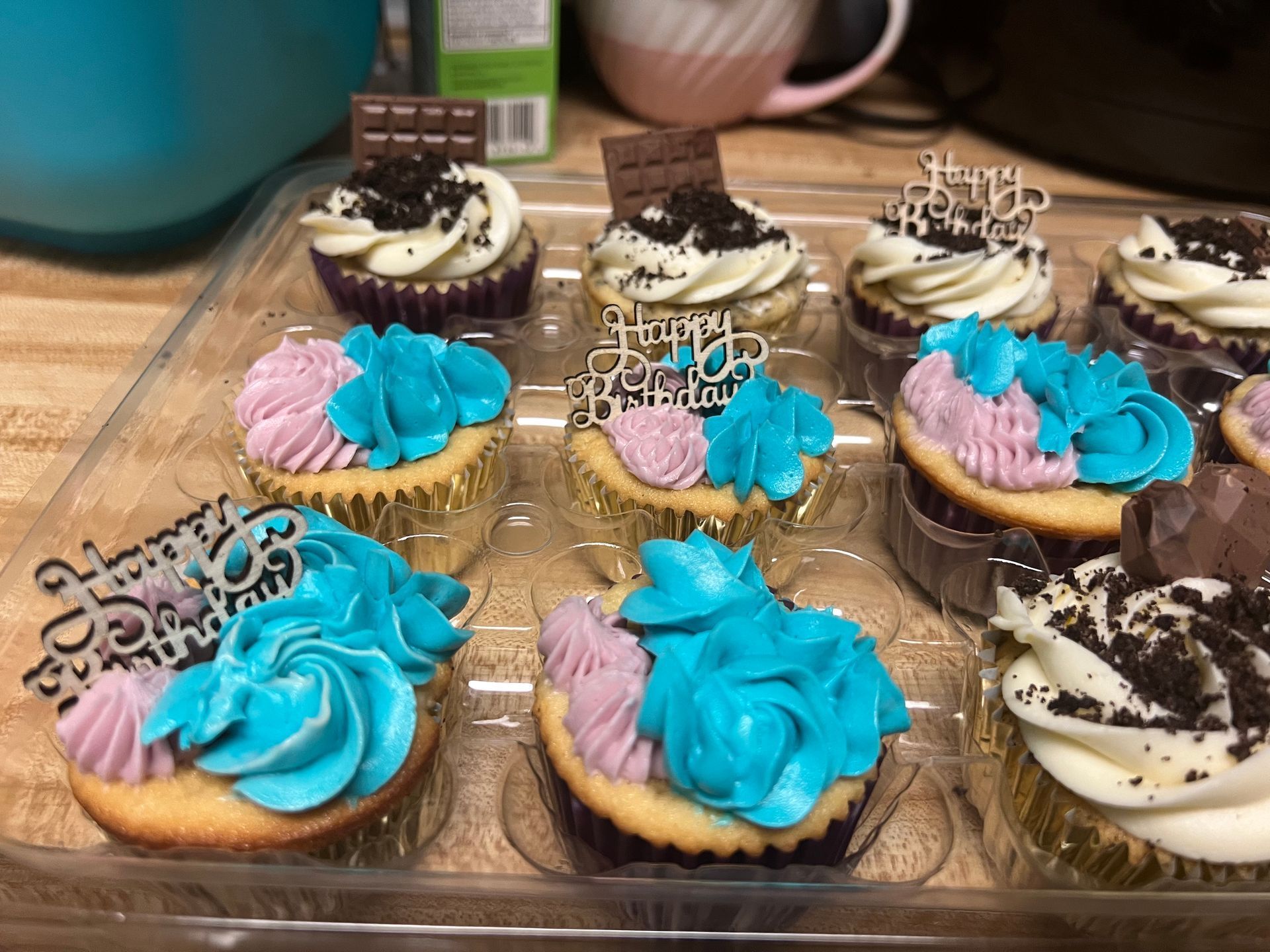 Tray of colorful decorated mini tarts with pink, blue, and chocolate frosting on a wooden table