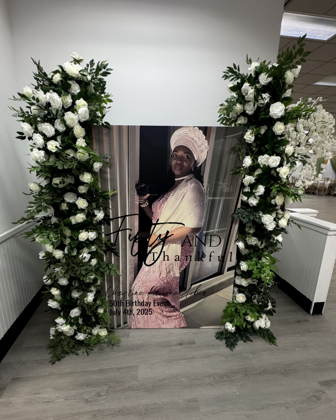 Floral memorial display with white flowers framing a portrait poster and pink drape