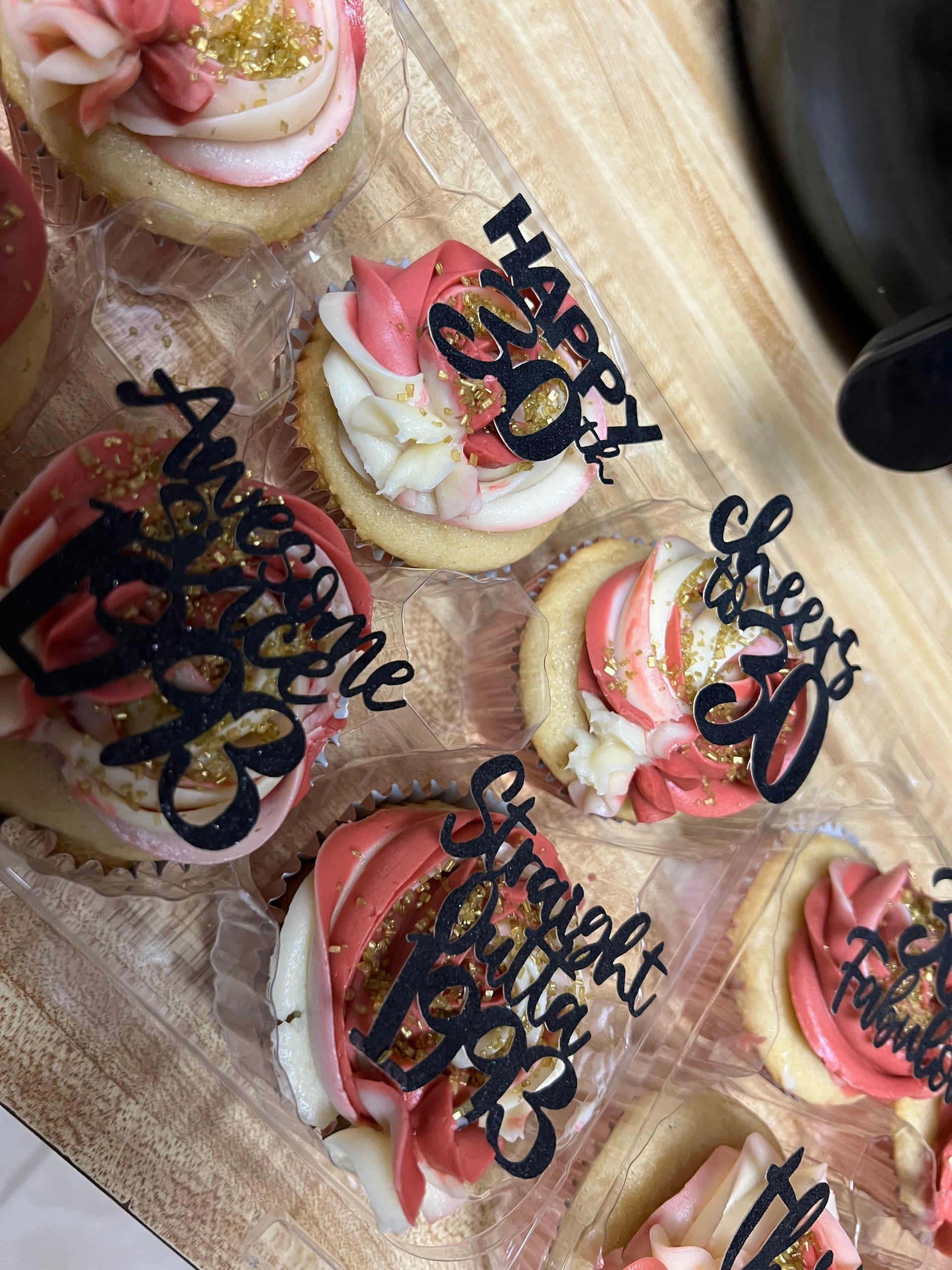 Assorted decorated cookies on a wooden board, topped with pink frosting and black script cake toppers.