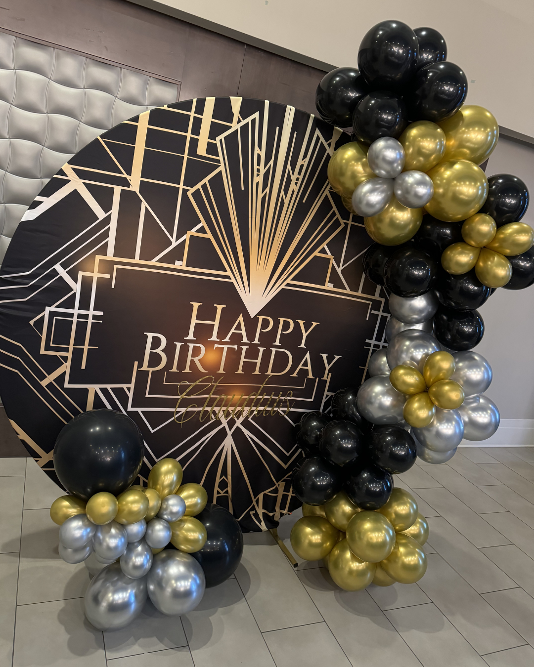 Black and gold birthday balloon display with a “Happy Birthday” sign and balloon clusters on the floor