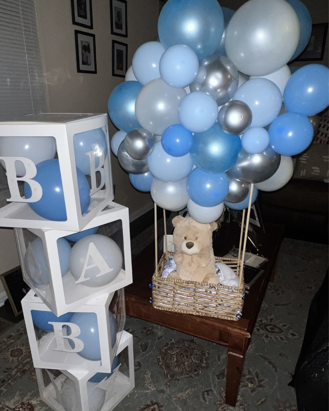Blue and white balloon display beside stacked blue monogram blocks and a teddy bear in a basket
