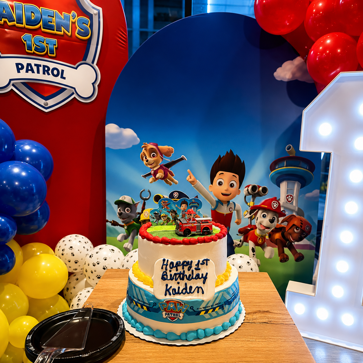 Paw Patrol birthday cake with balloons, blue backdrop, and a lit number 1 decoration