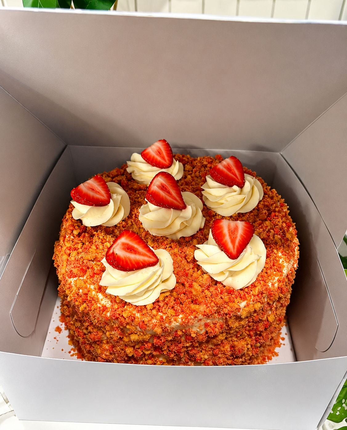 Square cake in a box, topped with swirled frosting and sliced strawberries.
