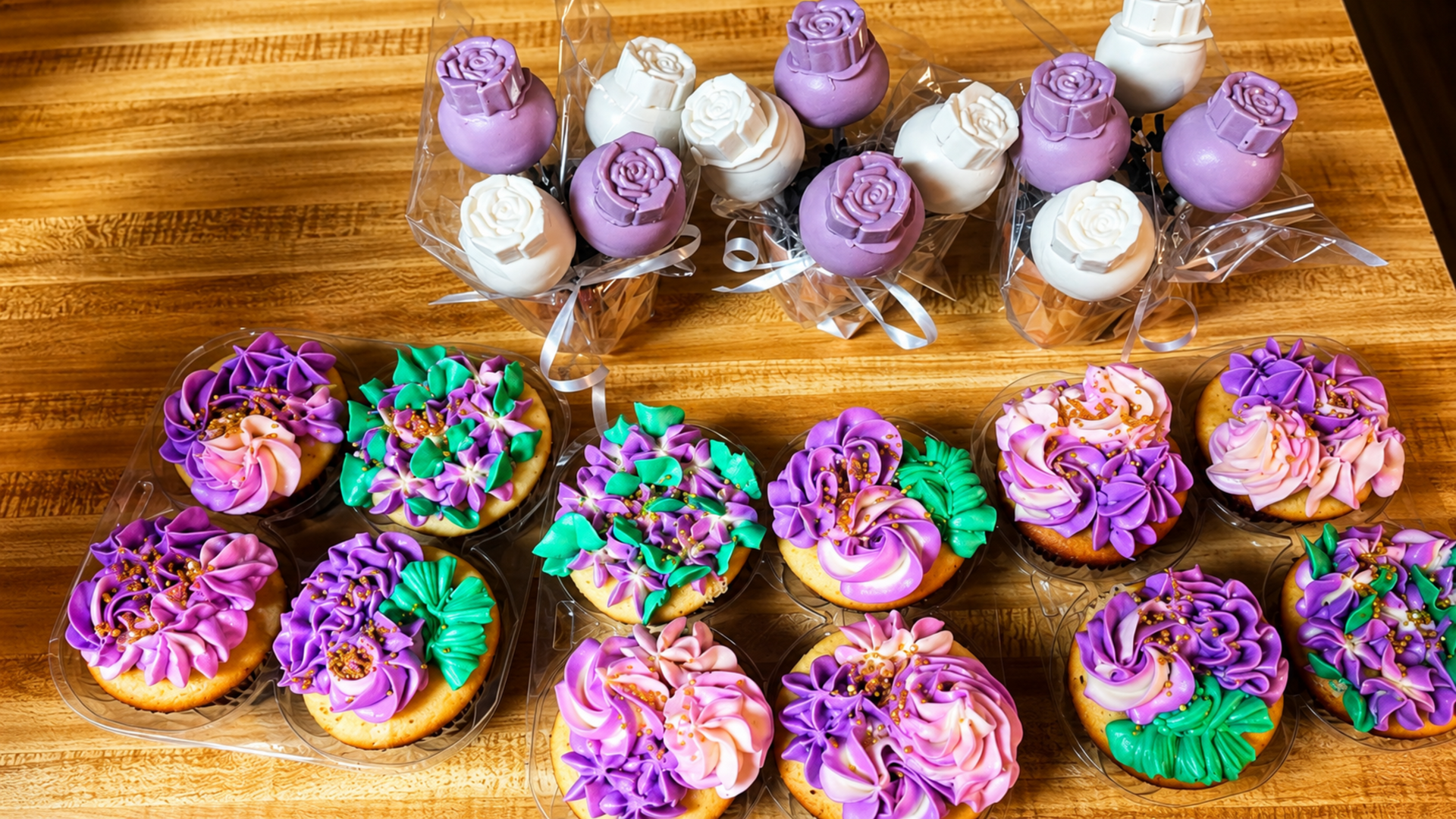 Assorted purple, white, and green frosted cupcakes arranged on a wooden table.