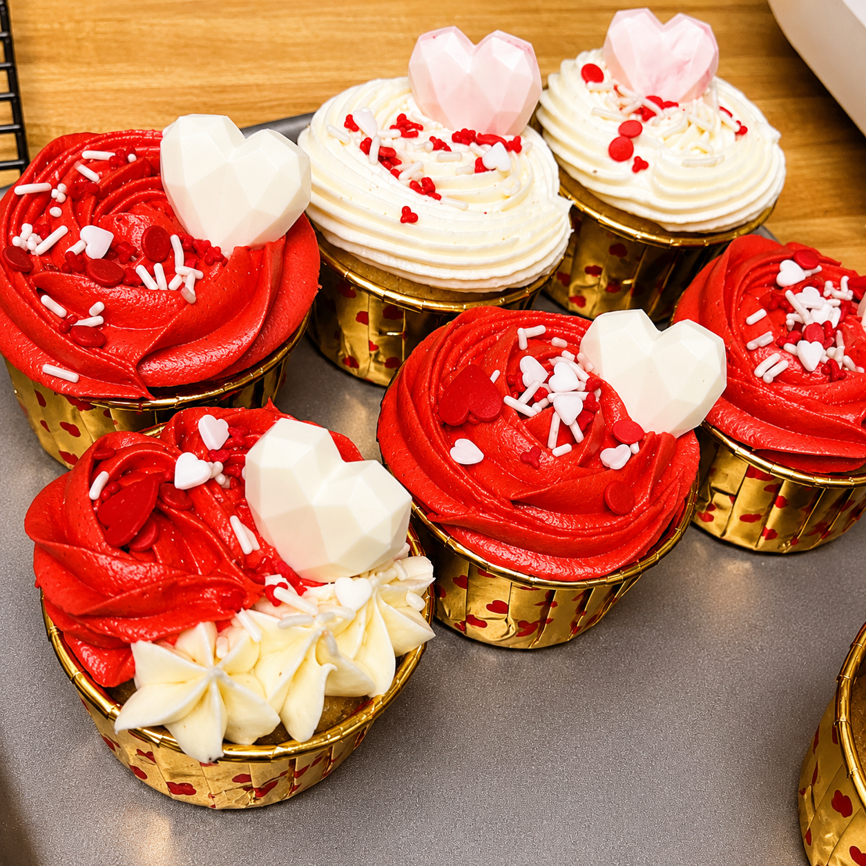 Red and white frosted cupcakes with heart toppers arranged on a tray