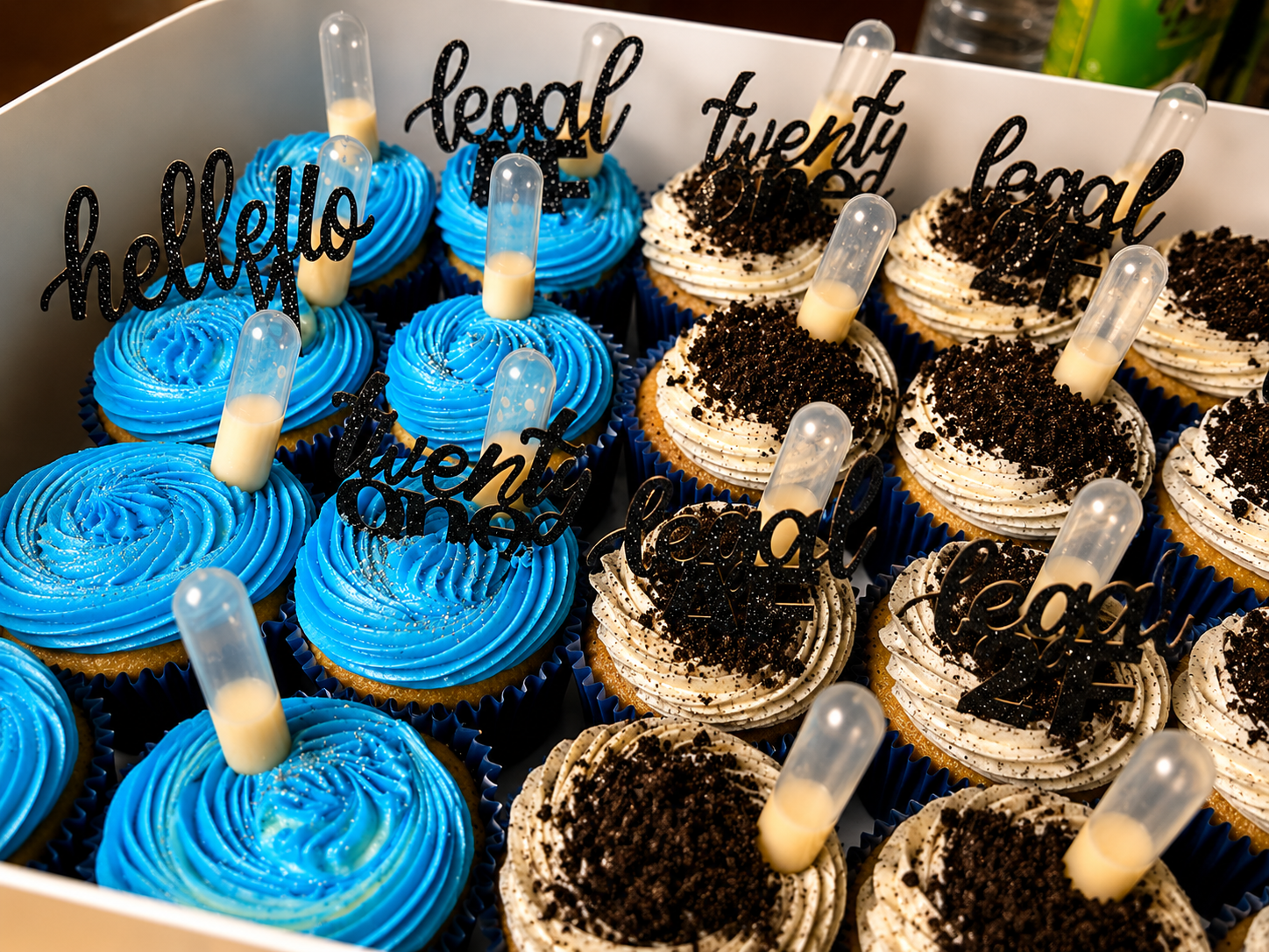 Tray of decorated blue and chocolate cupcakes with pipette toppers and black “legal” signs