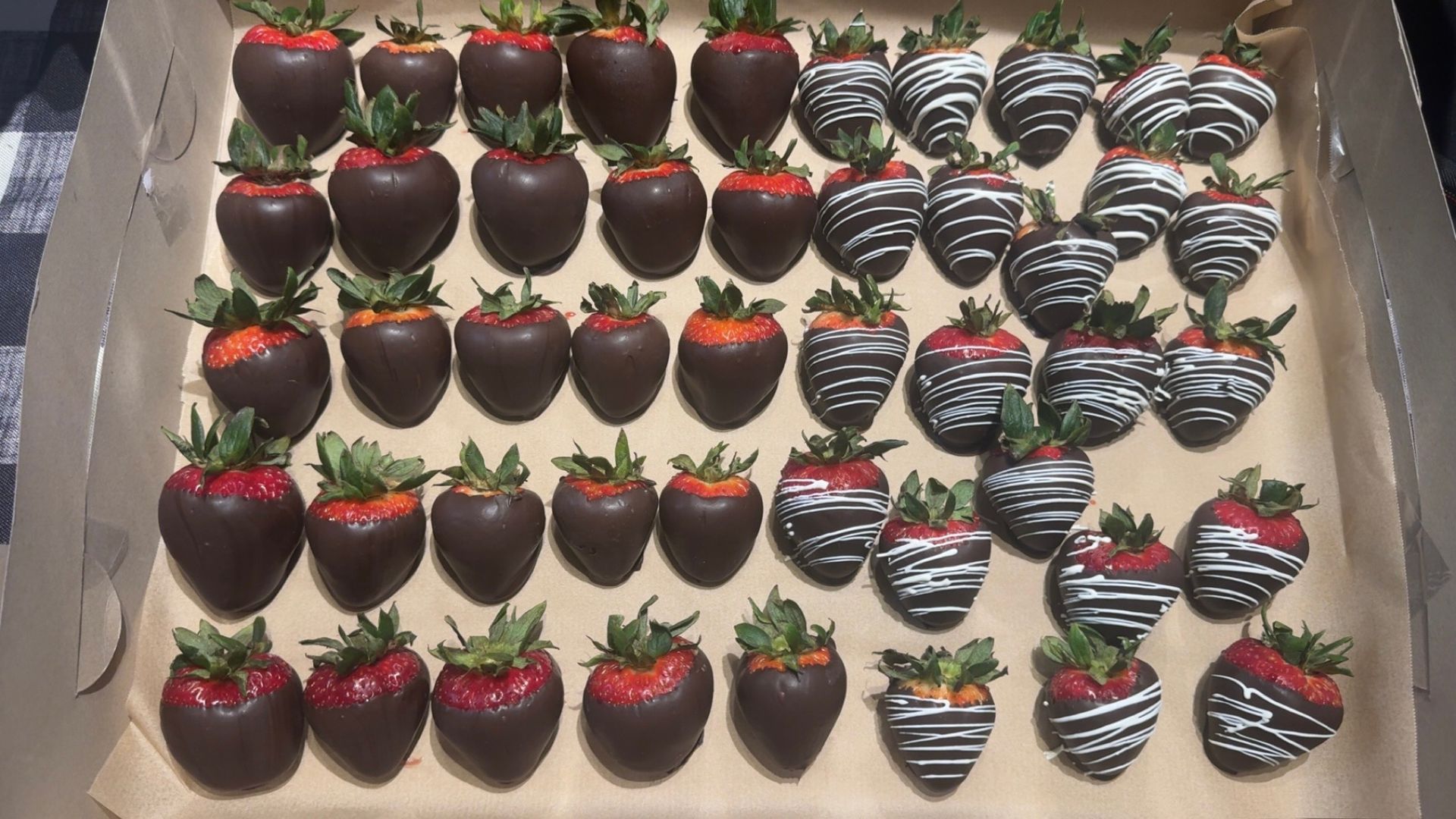 Box of chocolate-covered strawberries, some decorated with white and dark chocolate drizzle.