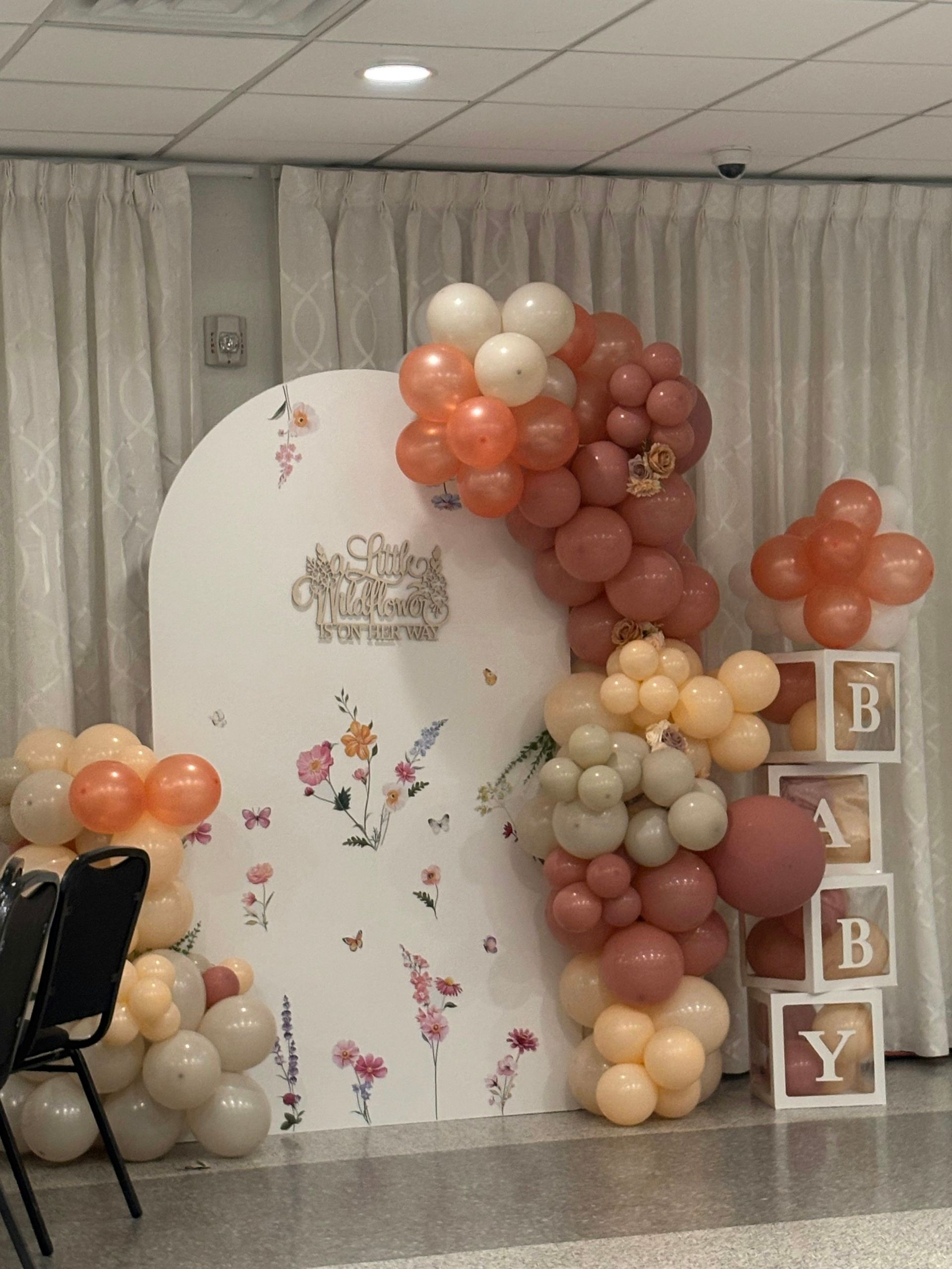 Balloon-decorated backdrop with a floral white panel and stacked “B Y” blocks at a celebration setup