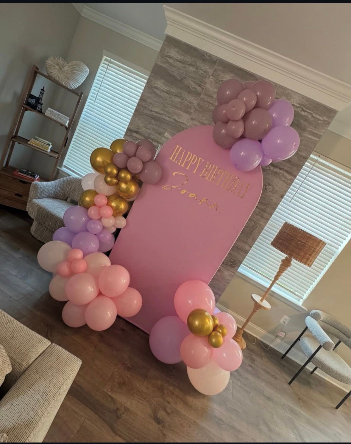 Pink and lavender balloon display with a sign in a home living room