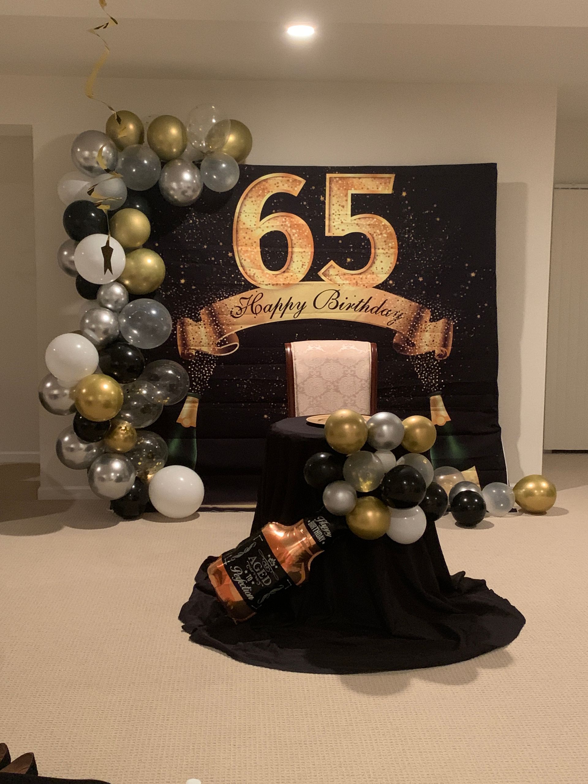 65th birthday party display with gold and black balloon decor, cake table, and balloons on the floor