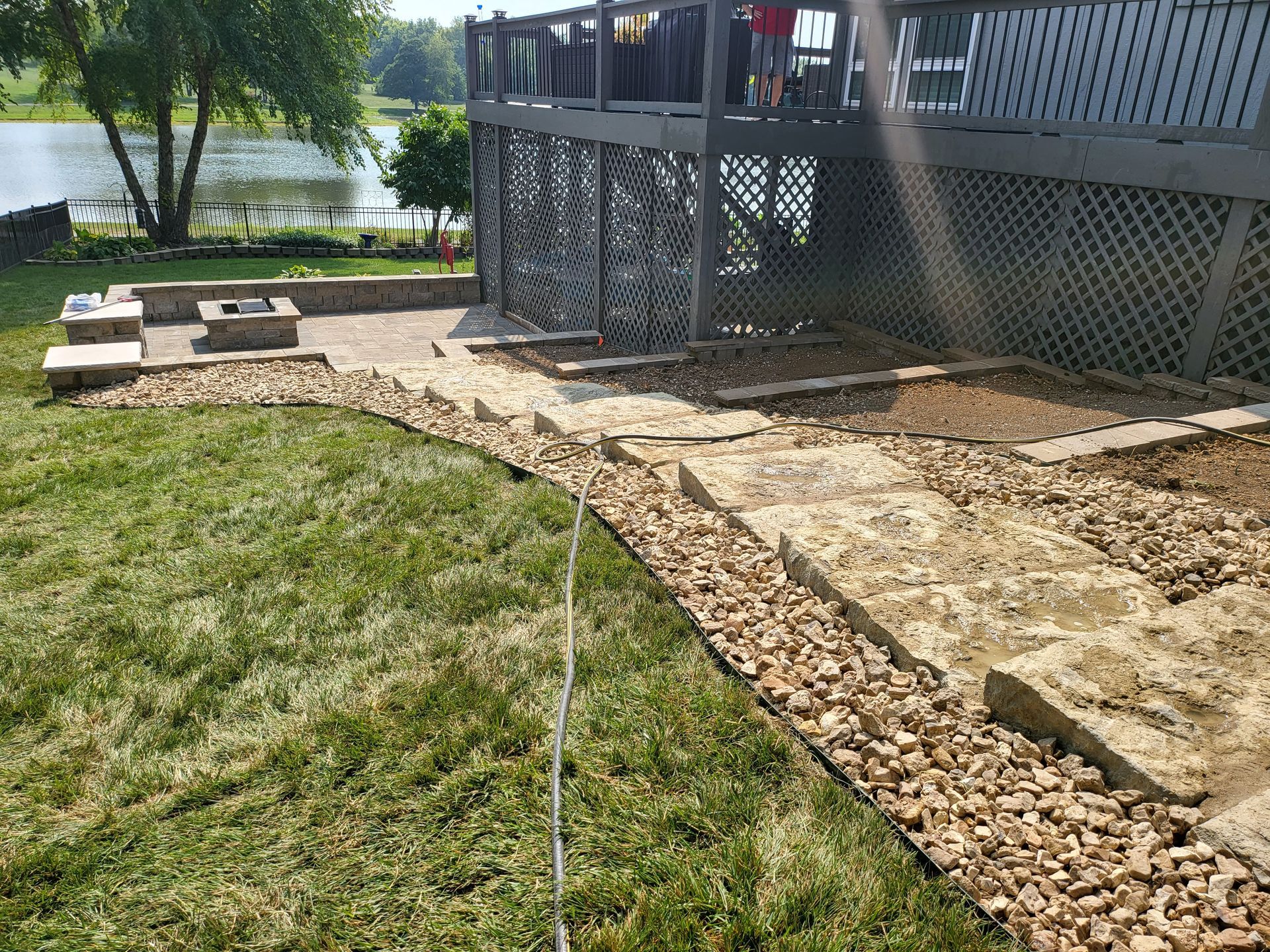 Gravel path beside a raised wooden deck and lake, bordered by grass and stone edging.