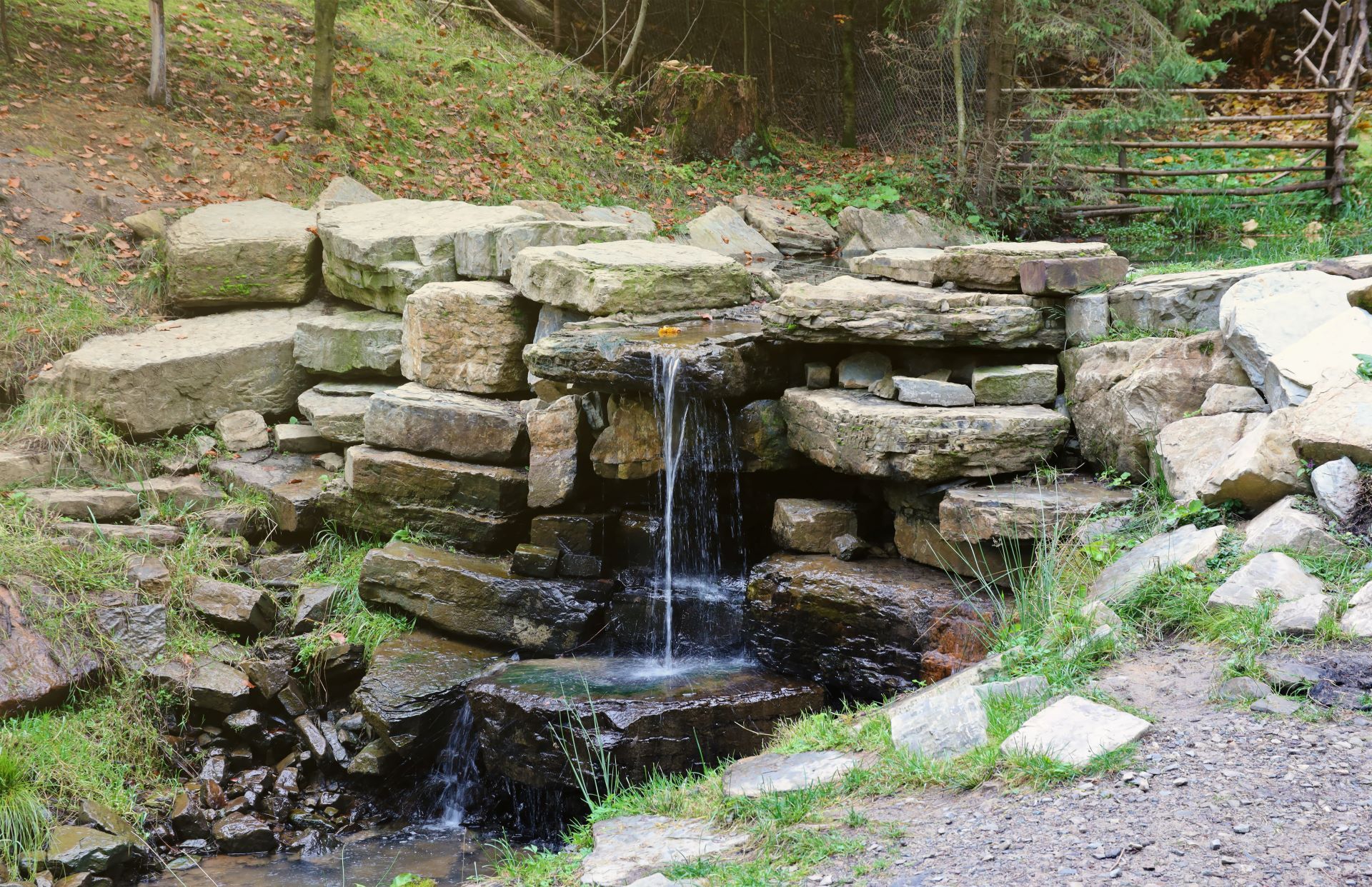 Small stone waterfall trickling into a pond in a garden with rocks and greenery