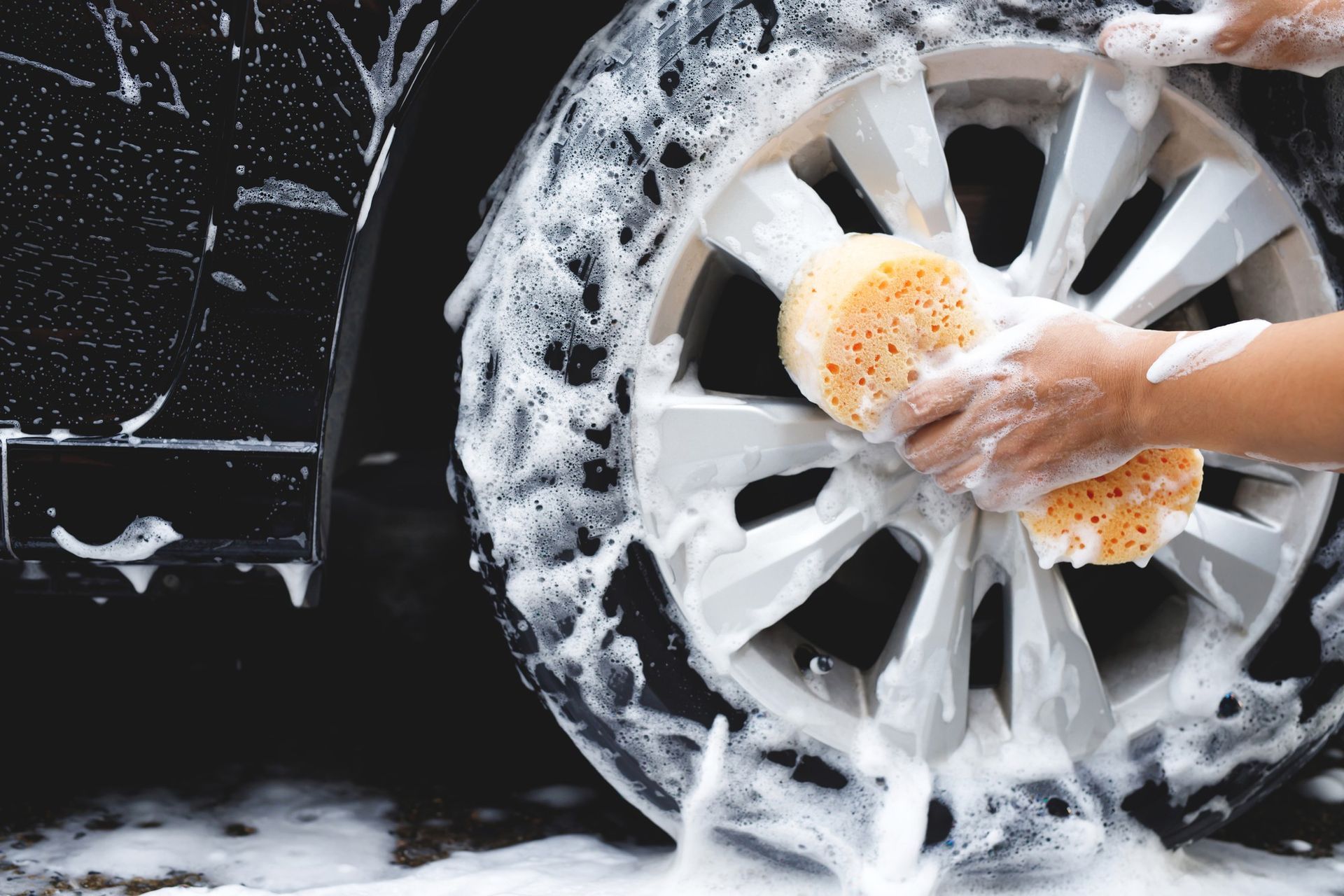 A person is washing a car wheel with a sponge.
