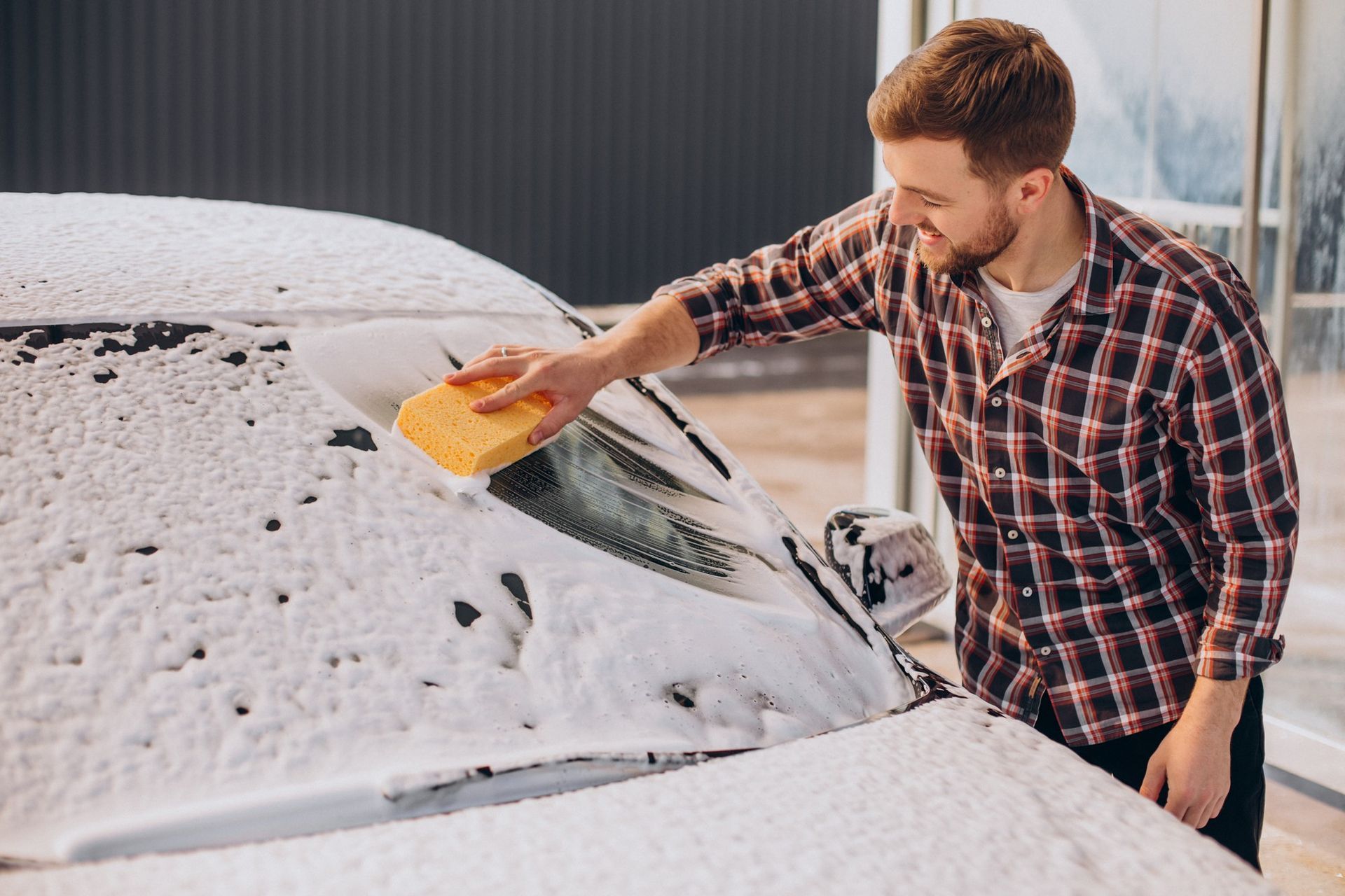 A man is washing his car with a sponge.