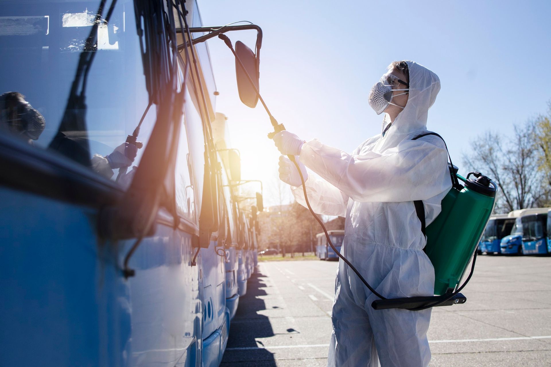 A man in a protective suit is disinfecting a bus in a parking lot.