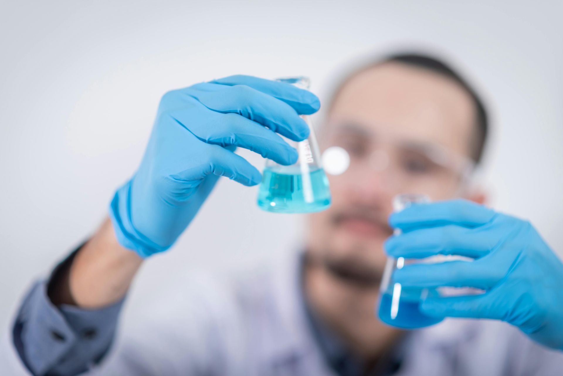 A scientist is holding a beaker with a blue liquid in it.