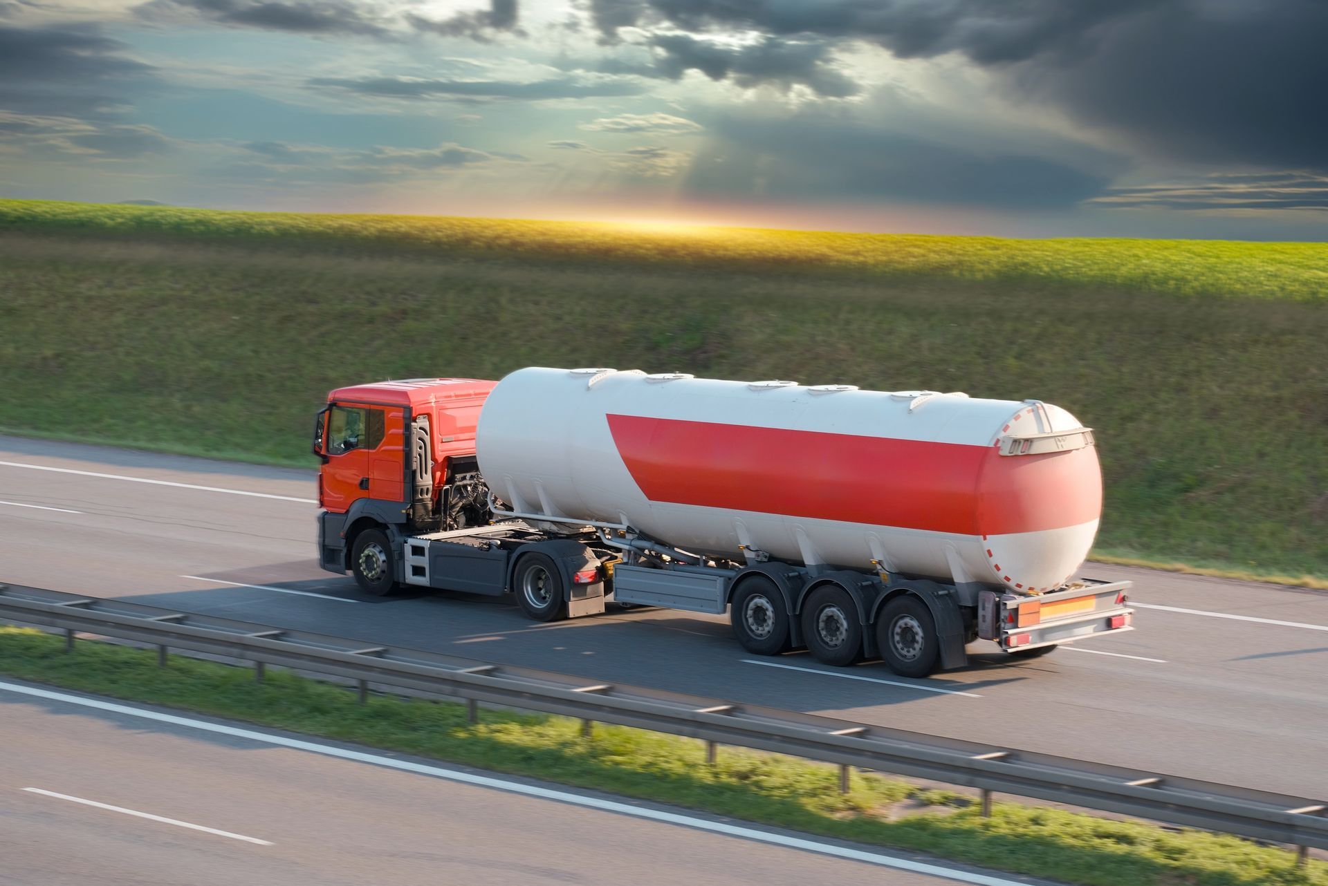 A red and white tanker truck is driving down a highway.