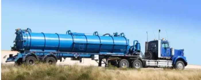 A blue semi truck (pump truck) is driving down a dirt road.