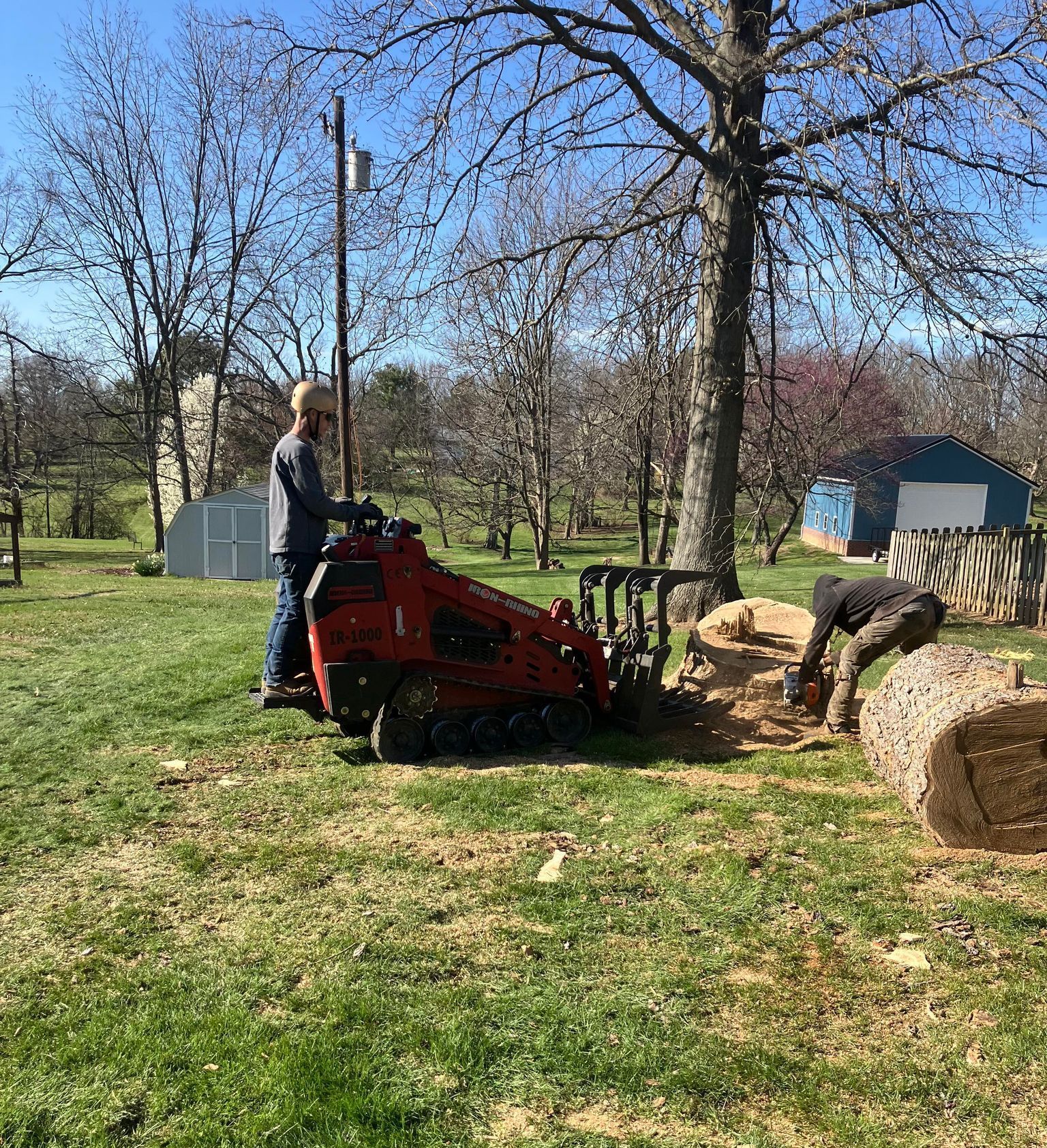A man is standing next to a red machine in a grassy field.