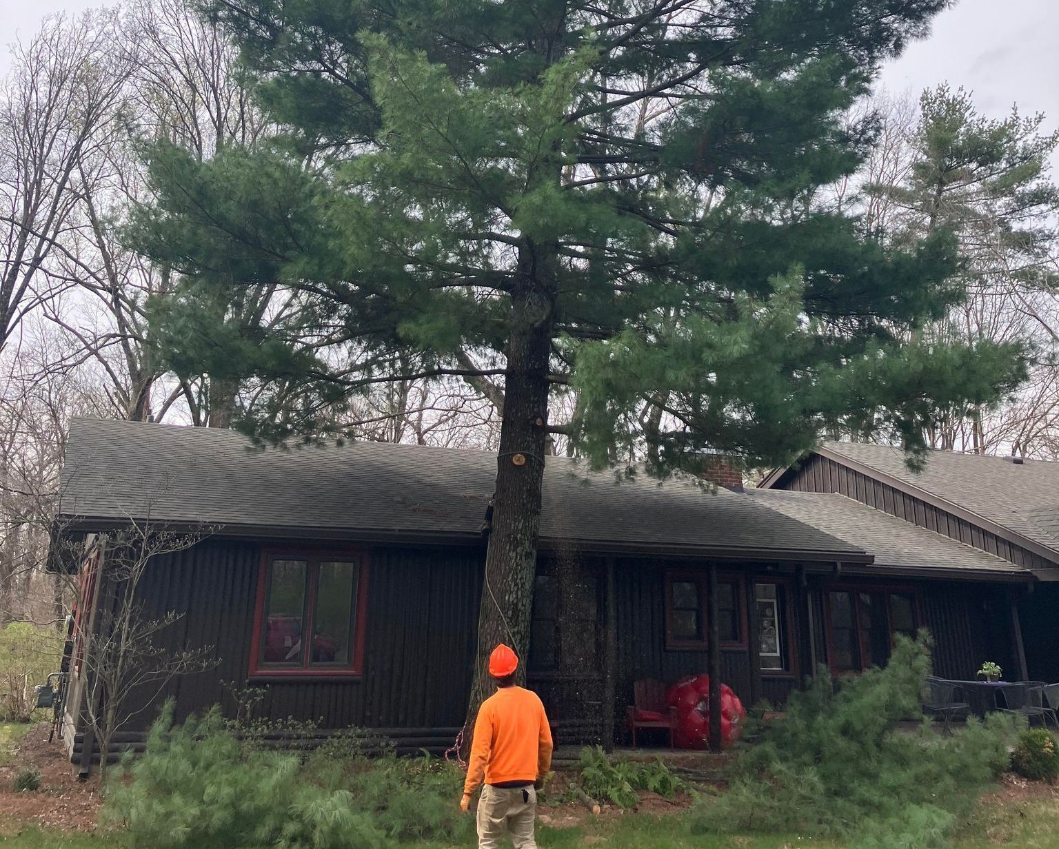 A man in an orange shirt is standing in front of a house