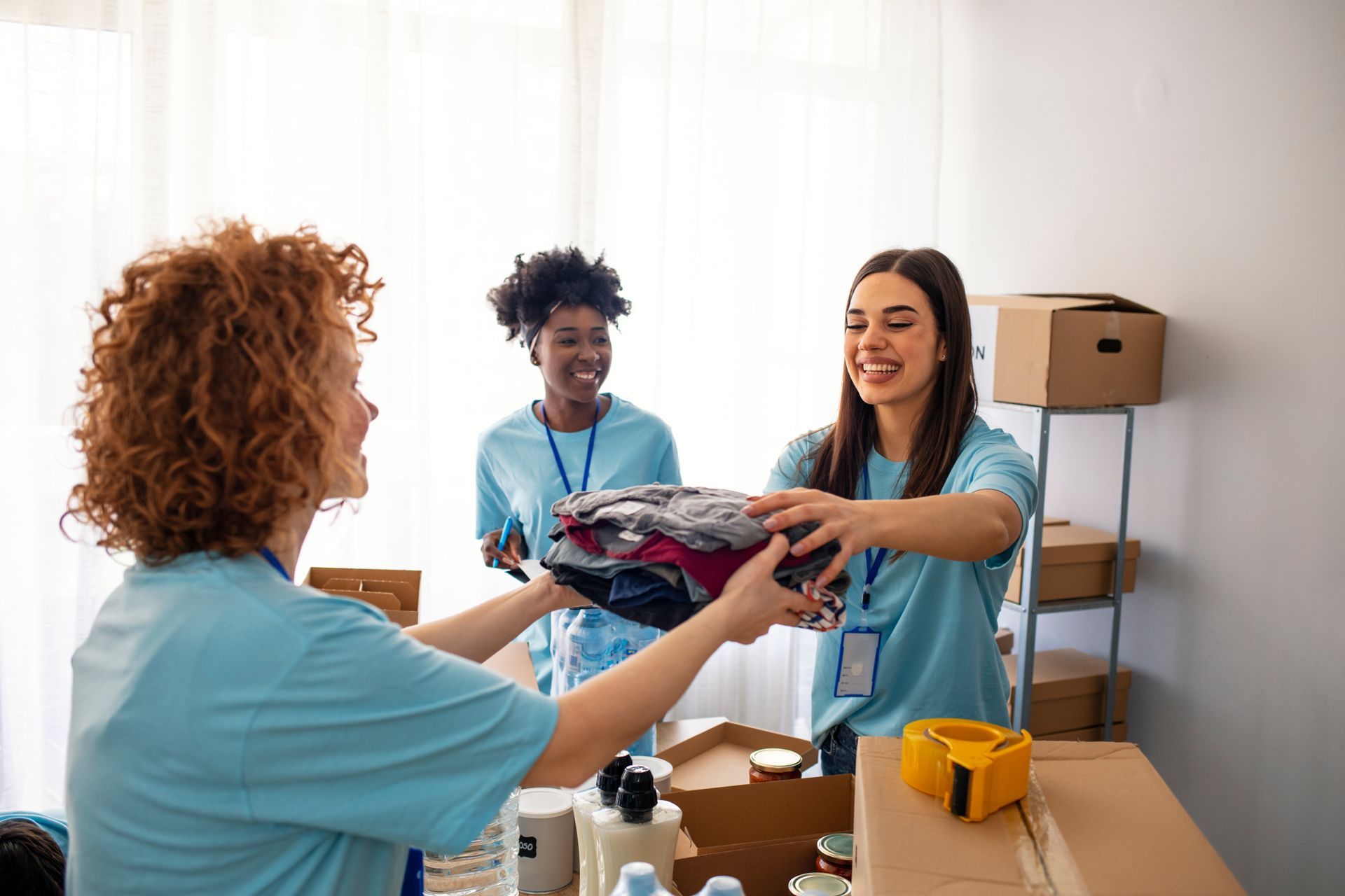 Volunteers packing and handing folded clothes in a donation center