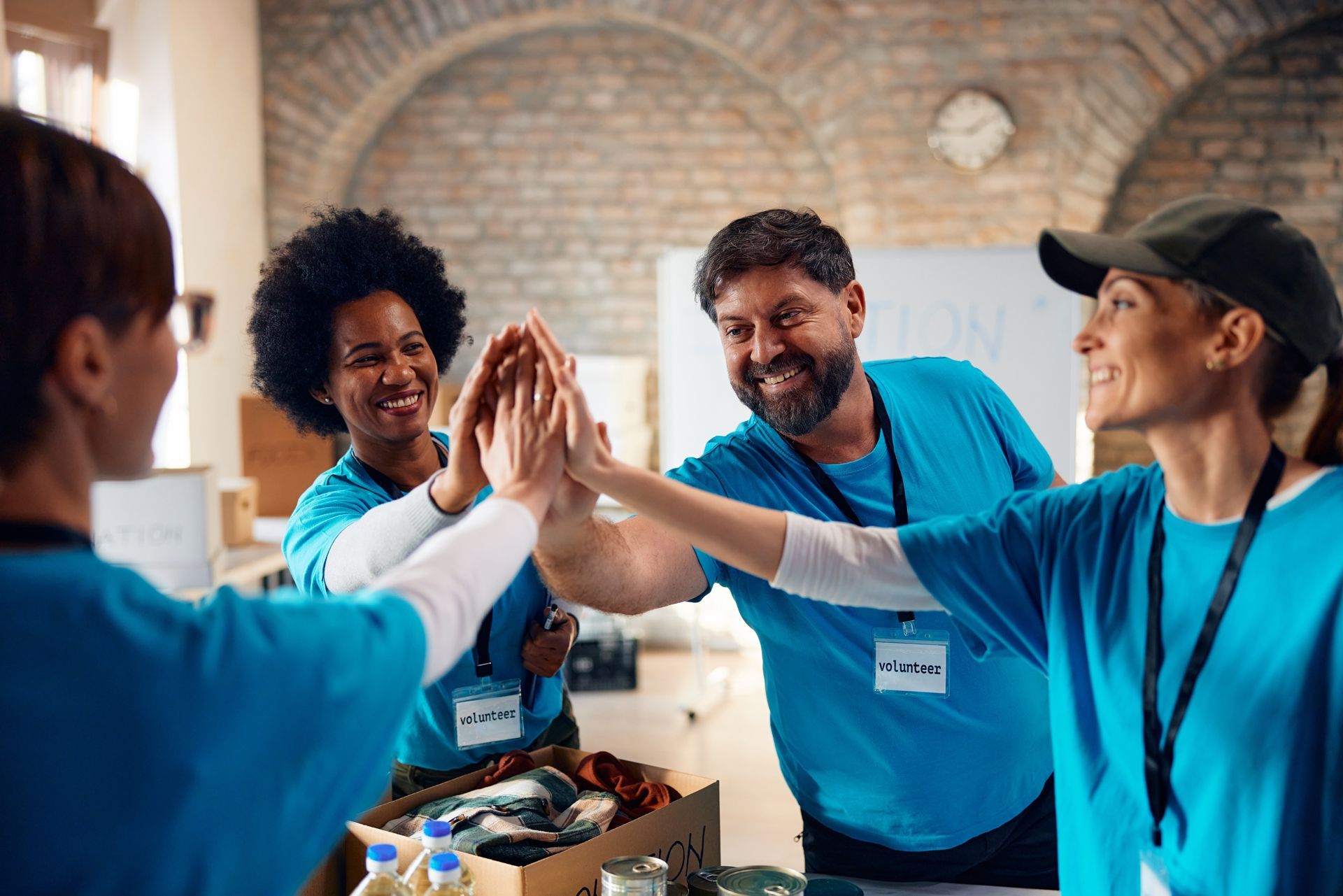 Volunteers in blue shirts high-five at a food bank table with boxed supplies