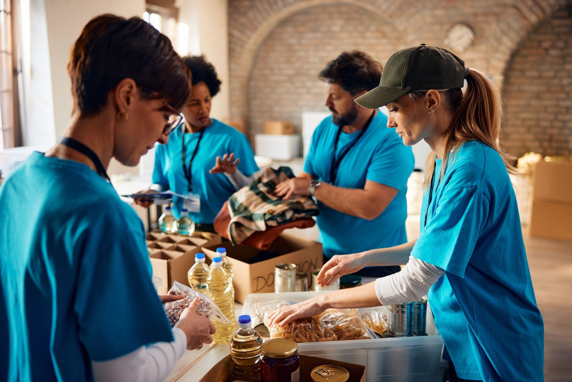 Volunteers in blue shirts packing food donations on a table in a brick room
