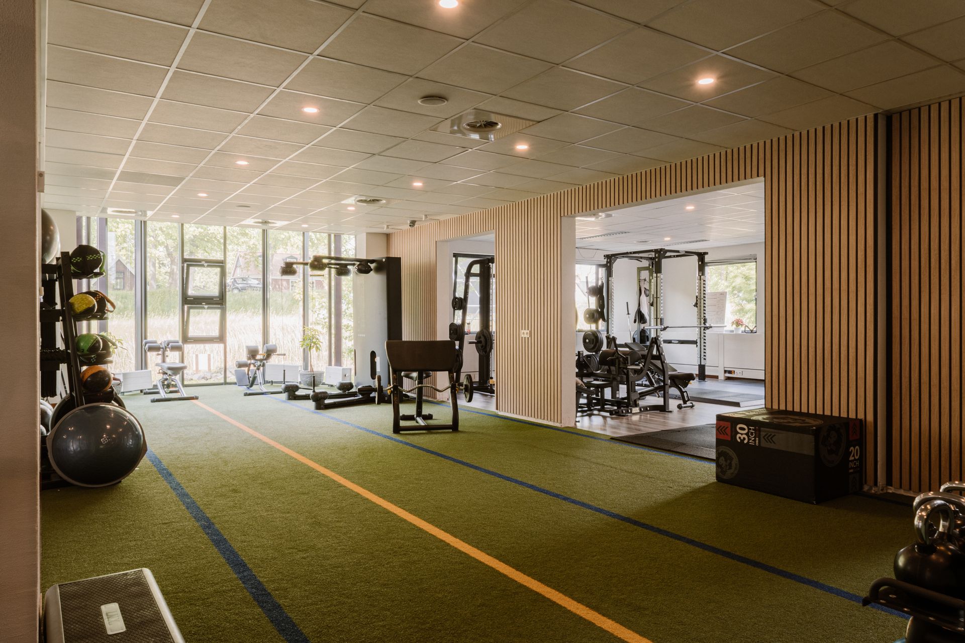 Modern fitnesscentrum met kunstgrasvloer, fitnessapparaten en grote ramen.