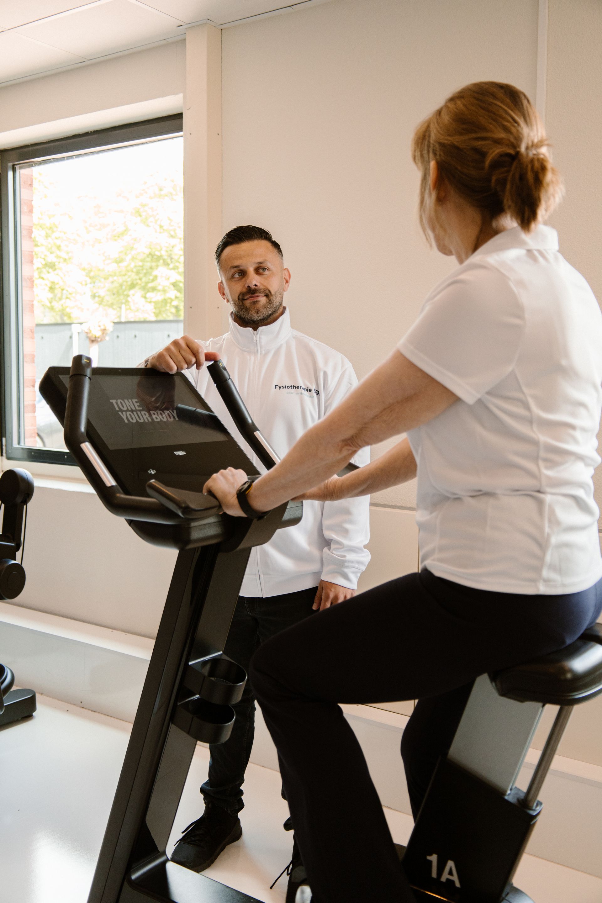 Twee mensen op hometrainers in een sportschool, die tijdens hun training met elkaar praten.