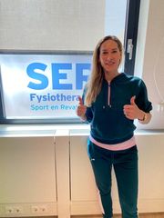 Vrouw steekt haar duim omhoog voor een bord van SER Physiotherapy Sport en Bewegen.