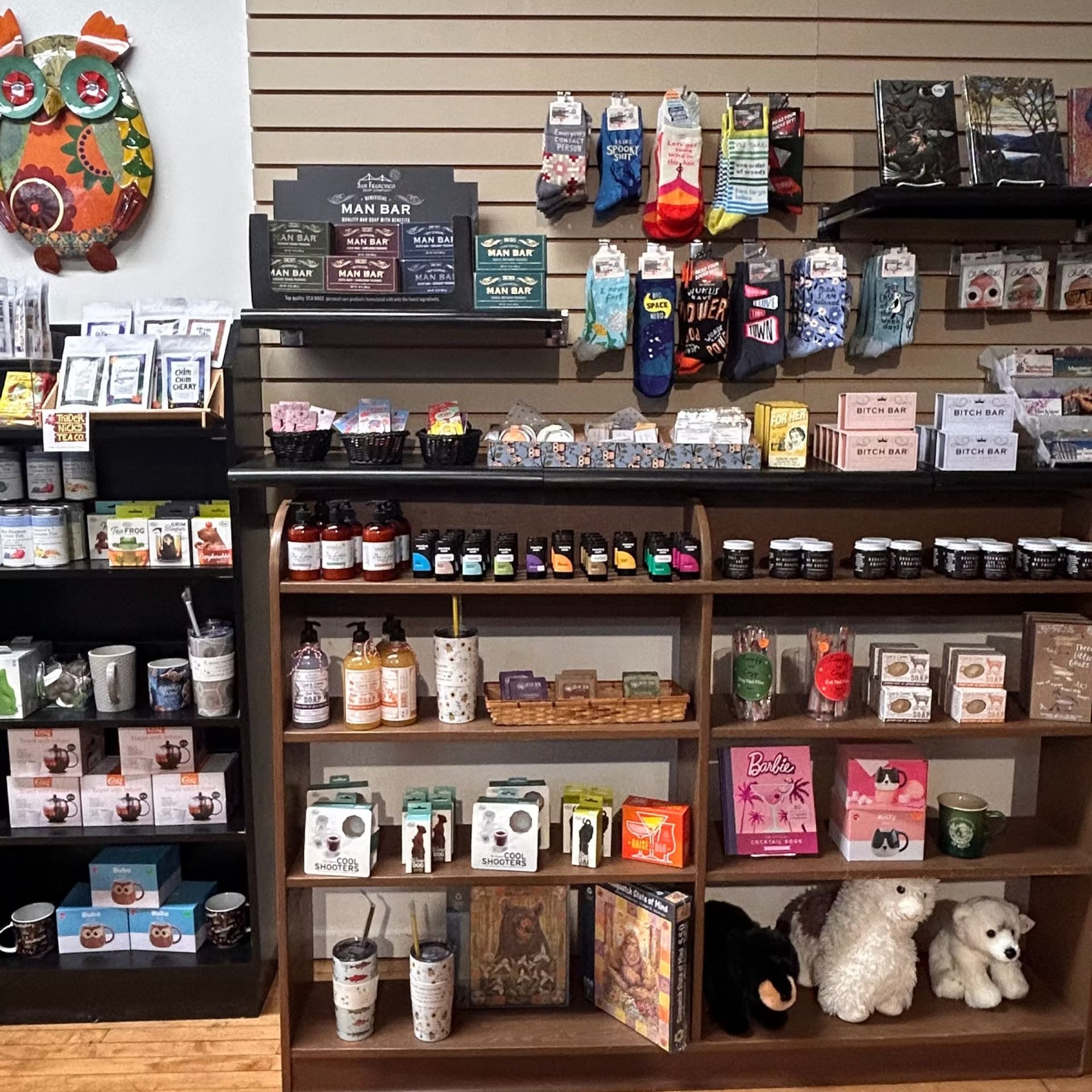 Retail display shelves with colorful pet products, treats, toys, and plush animals on a black wall shelf.