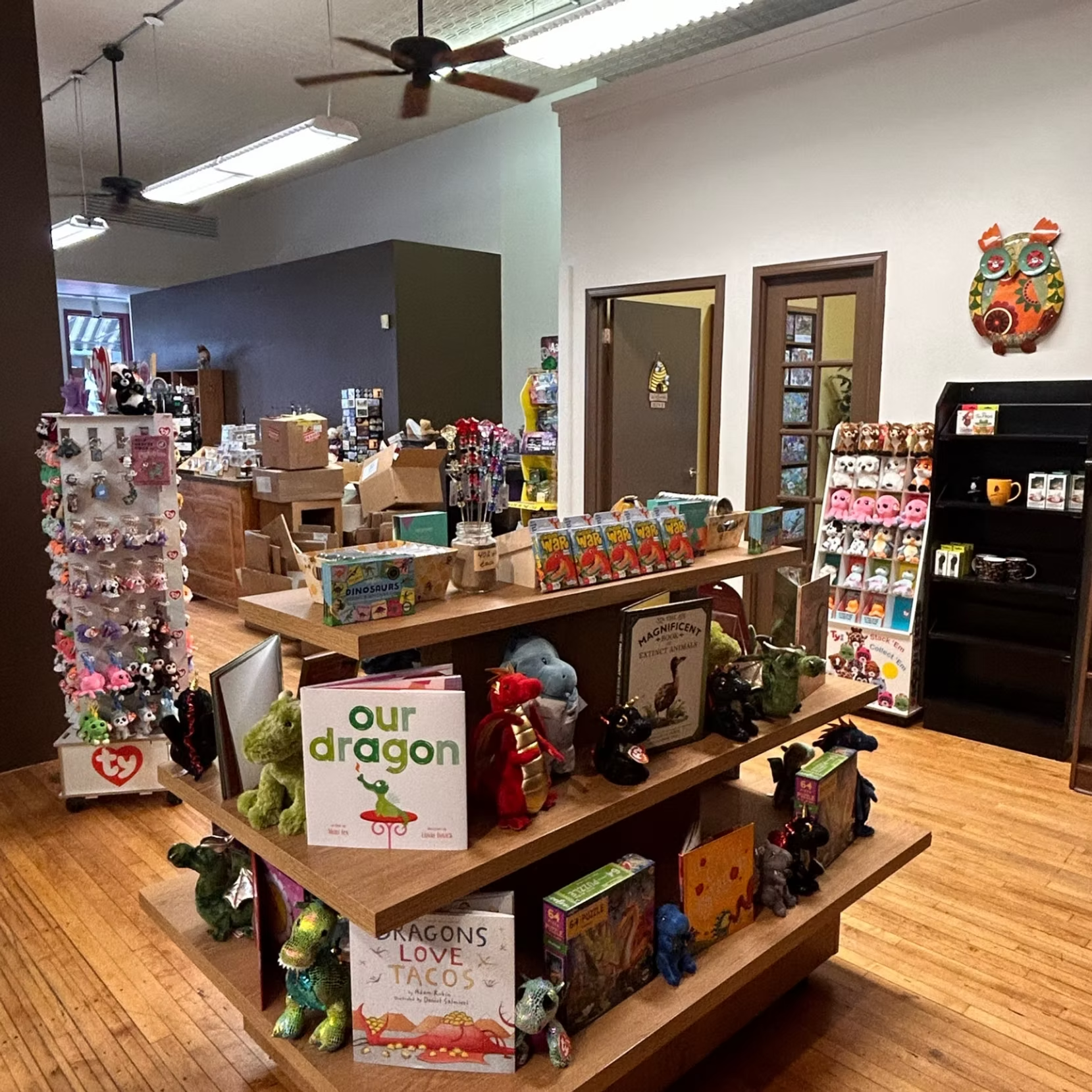 Toy store aisle with shelves of colorful plush toys, books, and gifts under ceiling fans and bright lights