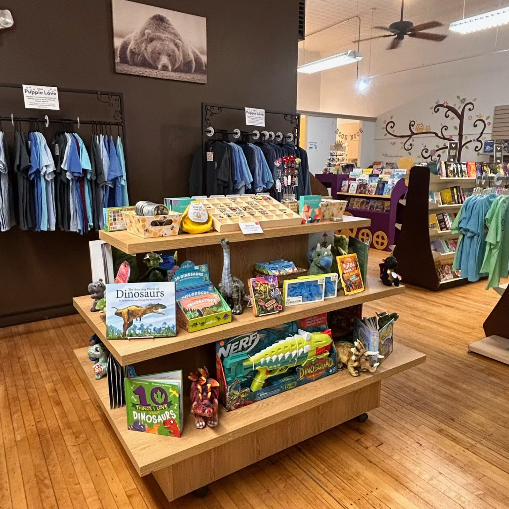 Gift shop with wooden display tables, colorful souvenirs, and blue shirts hanging on the wall.