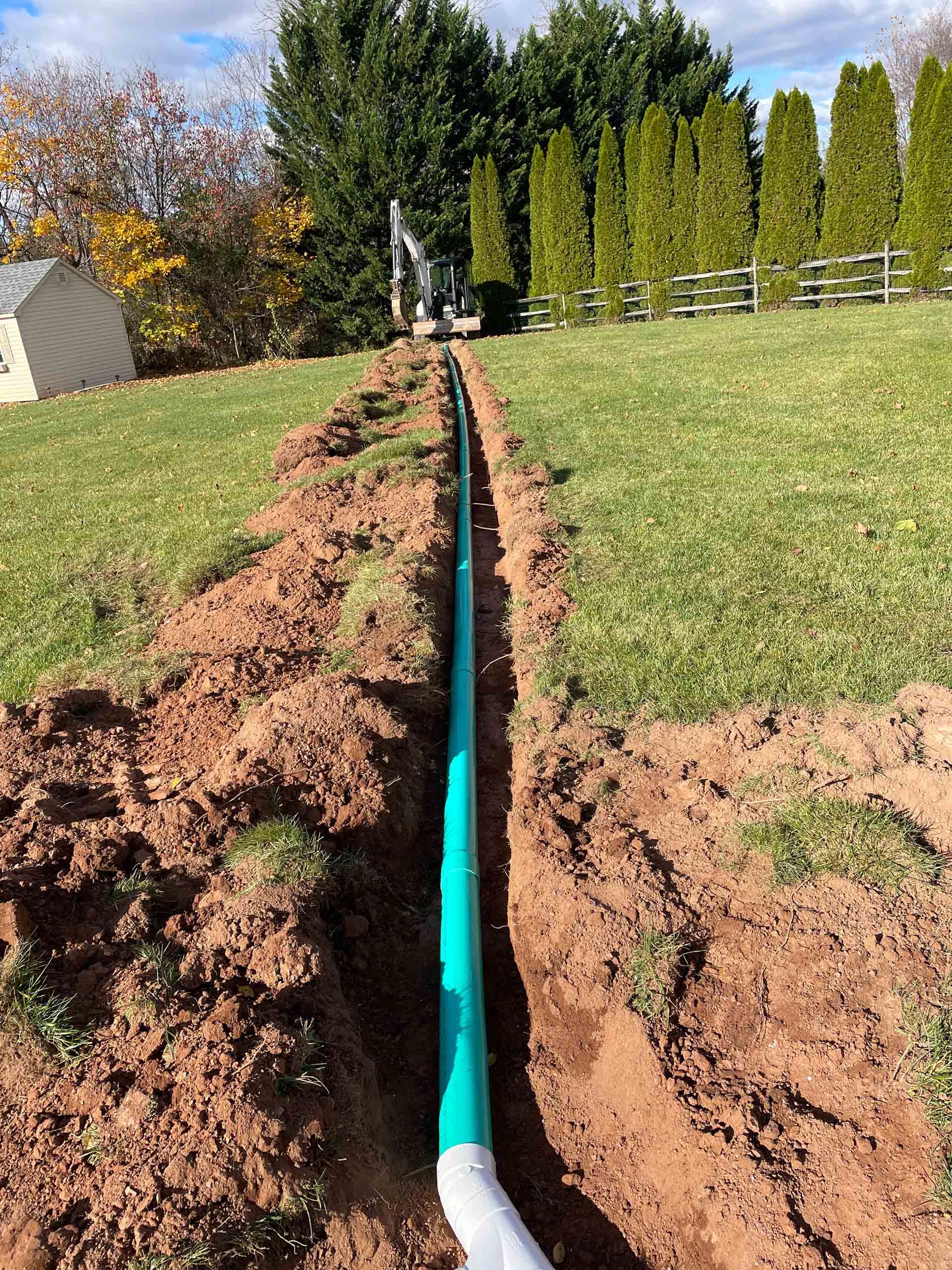 A green pipe is being installed in the dirt in a field.